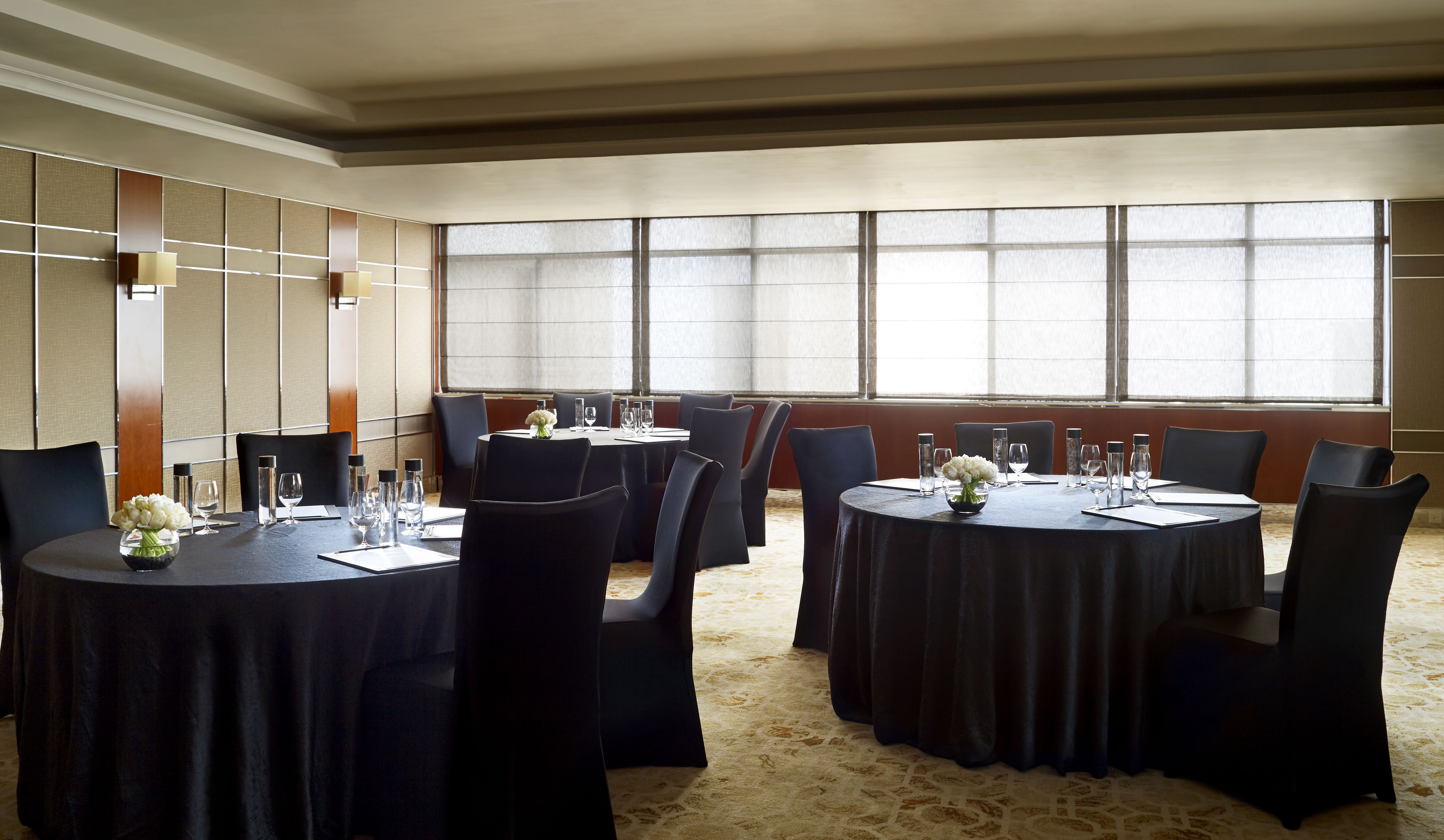 Un salón de conferencias con mesas redondas, sillas negras y ventanas amplias.