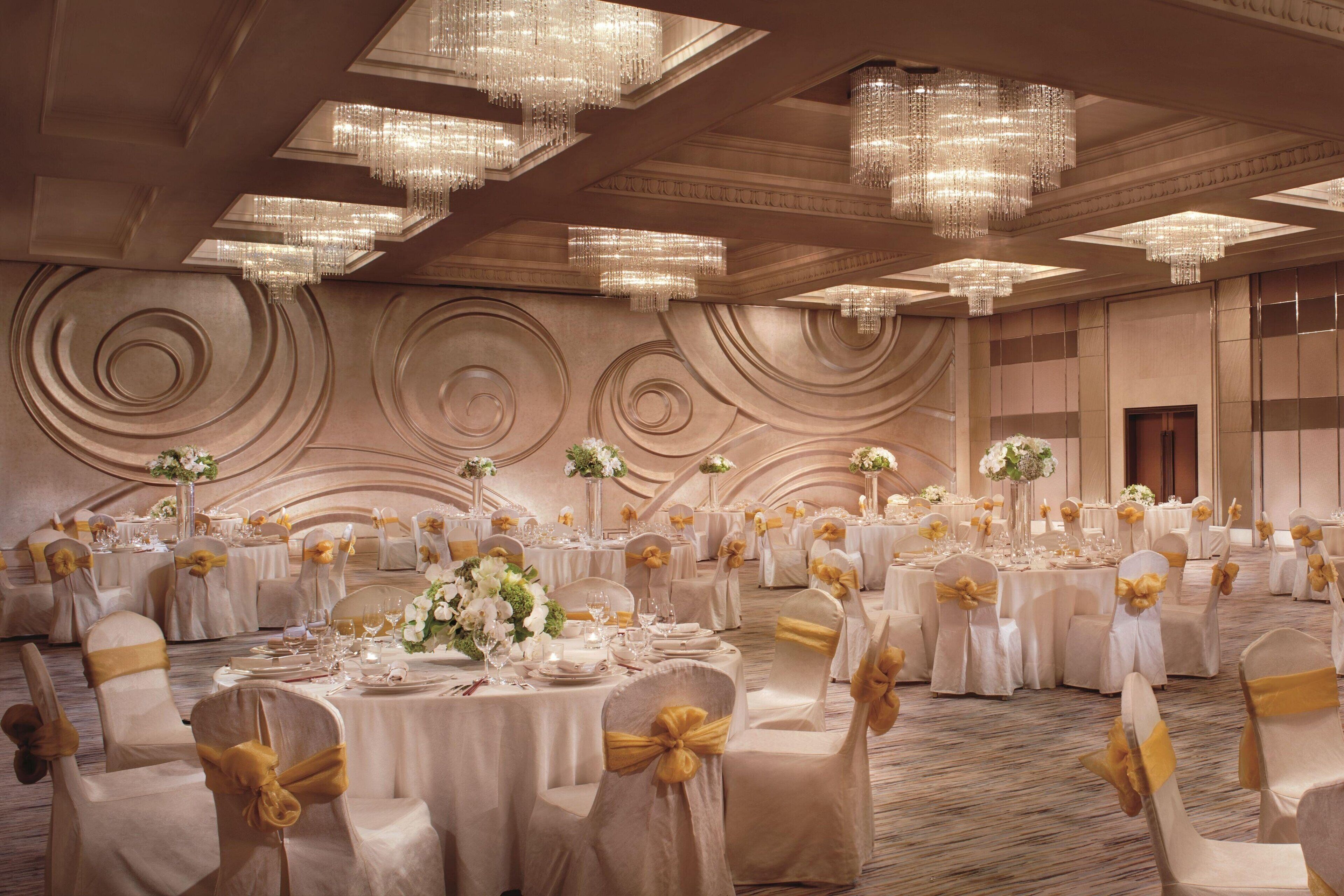 Un salón de banquetes con mesas redondas, sillas adornadas con cintas doradas y candelabros.