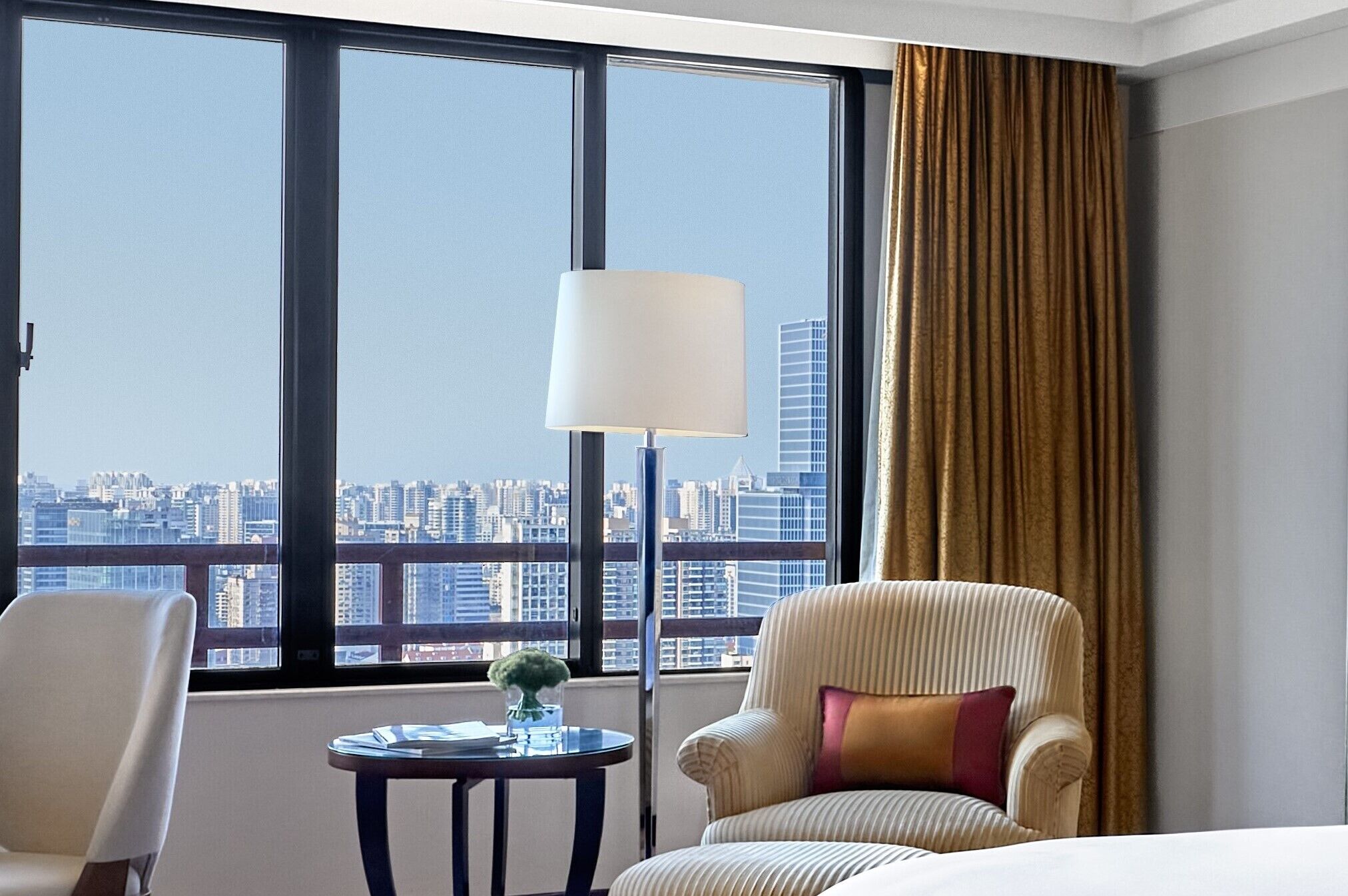 Une chambre d’hôtel avec une grande fenêtre, une lampe, une chaise et une petite table.