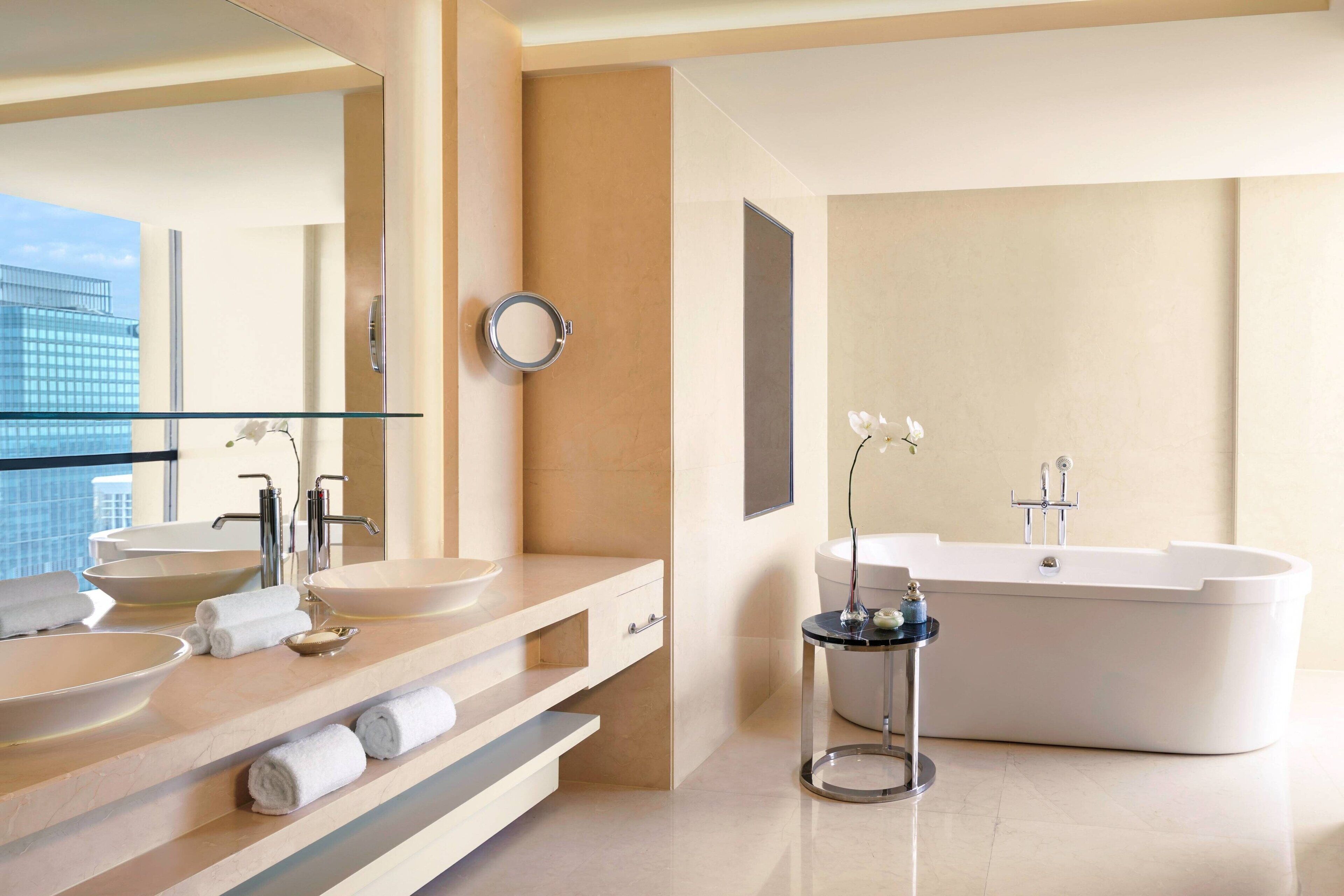 A modern bathroom with a large bathtub, two sinks, and a glass shower enclosure.