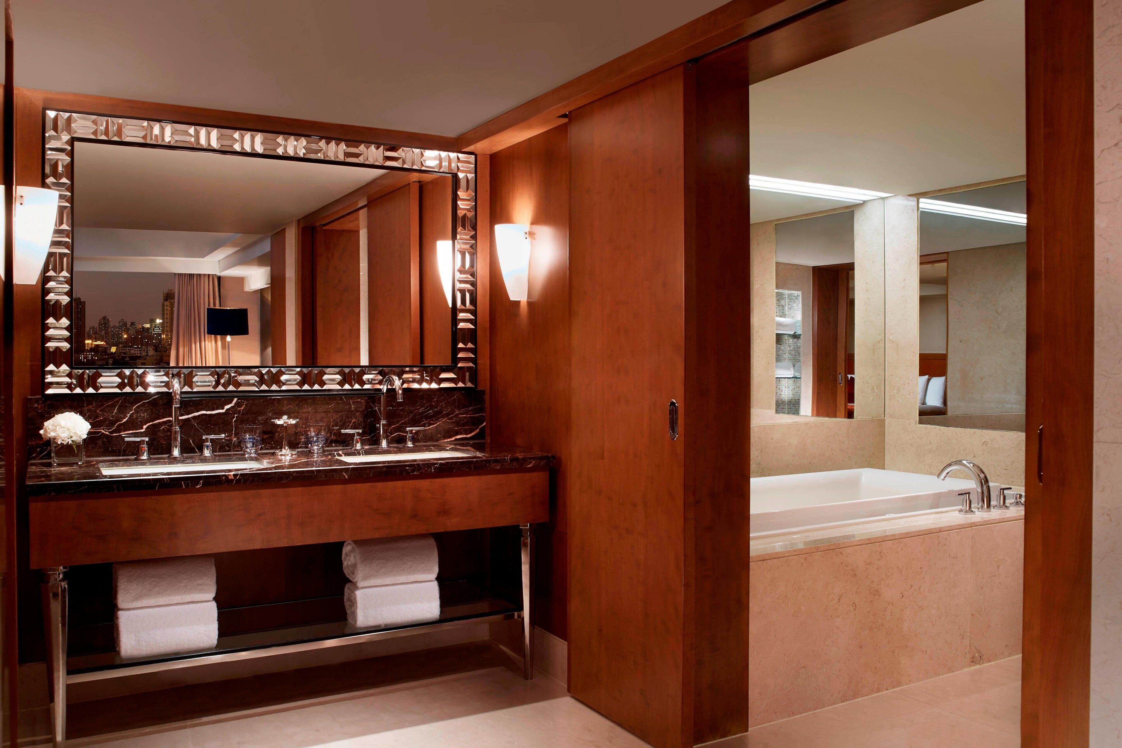 A modern bathroom with a large mirror, dual sinks, and a bathtub.