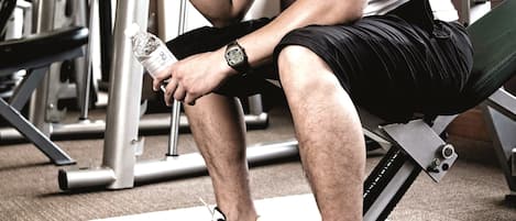 Un gimnasio con equipo de levantamiento de pesas, una banca y una persona usando una toalla.