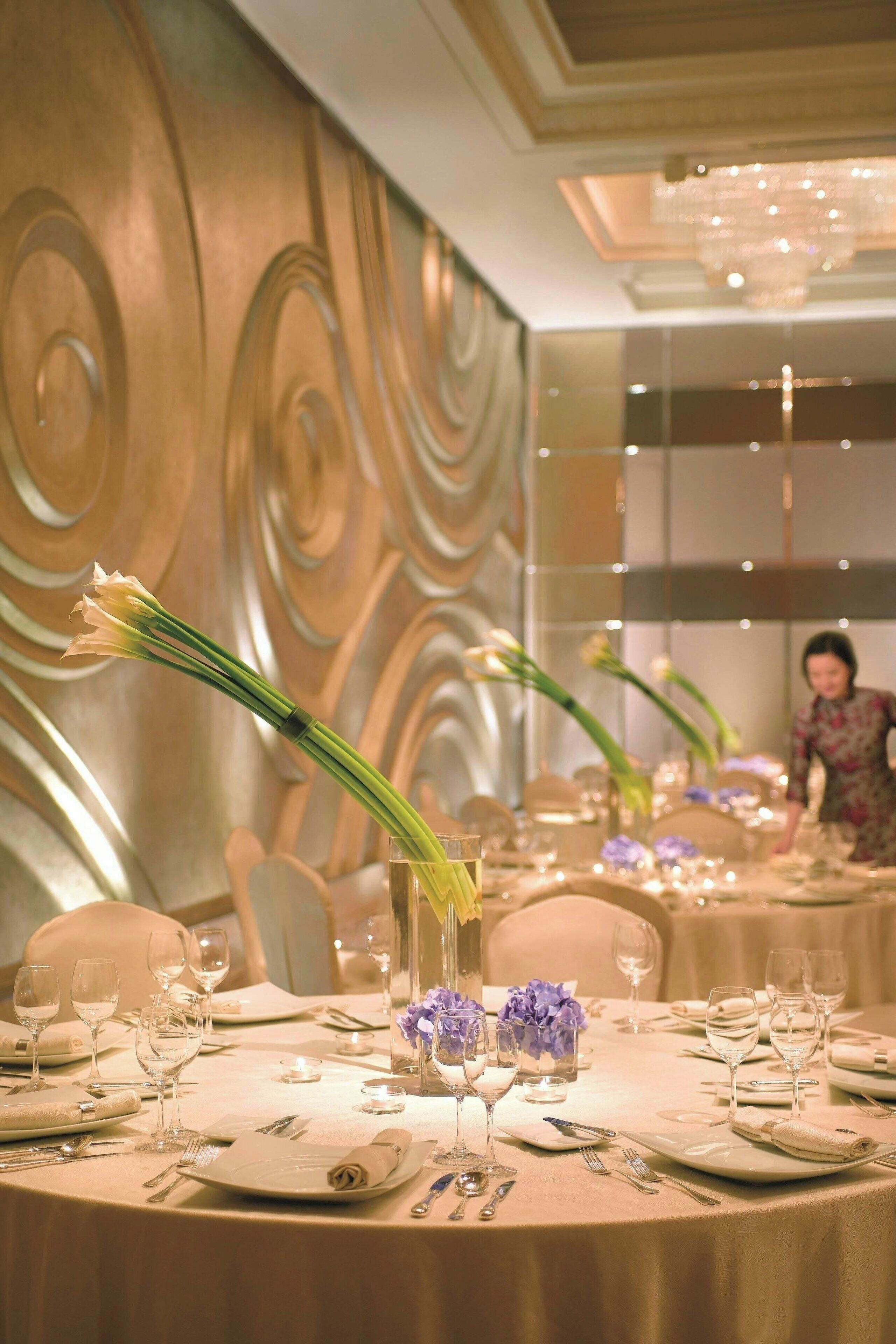 Mesa de banquete dispuesta para un evento formal, con una pared decorativa al fondo.