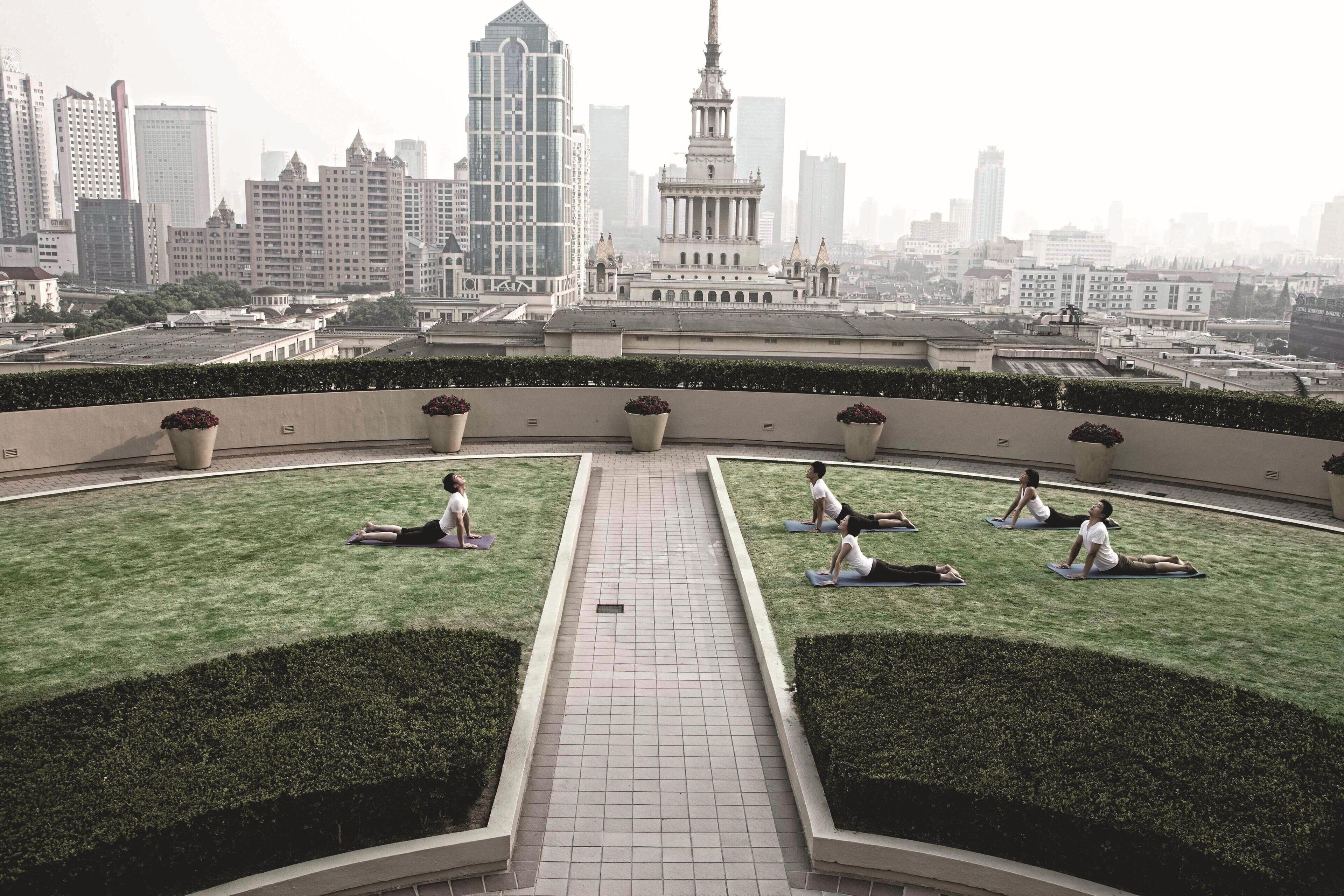 A rooftop garden with people doing yoga, surrounded by city buildings and a large monument in the background.