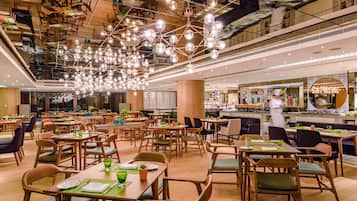 Un comedor amplio con varias mesas y sillas, un candelabro central y vista a la cocina al fondo.