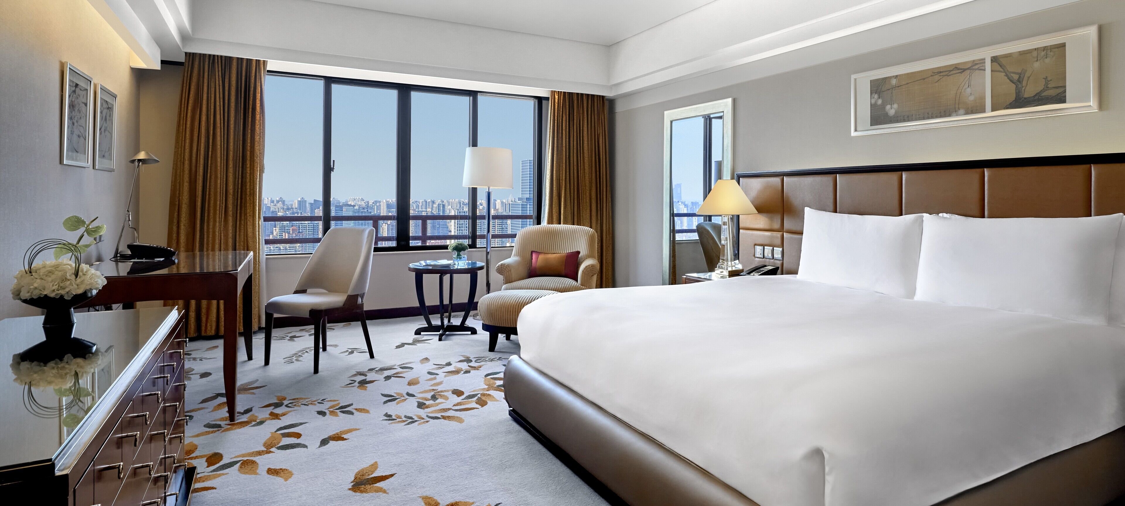 Habitación de hotel con una cama grande, un escritorio, dos sillas, una mesita y vistas a la ciudad.