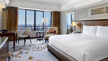 Habitación de hotel con una cama grande, un escritorio, dos sillas, una mesita y vistas a la ciudad.