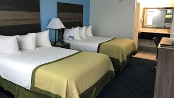 A hotel room with two beds, a desk, a chair, a lamp, and a bathroom with a mirror.