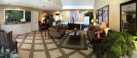 A hotel lobby with a reception desk, seating area, and a large mirror.