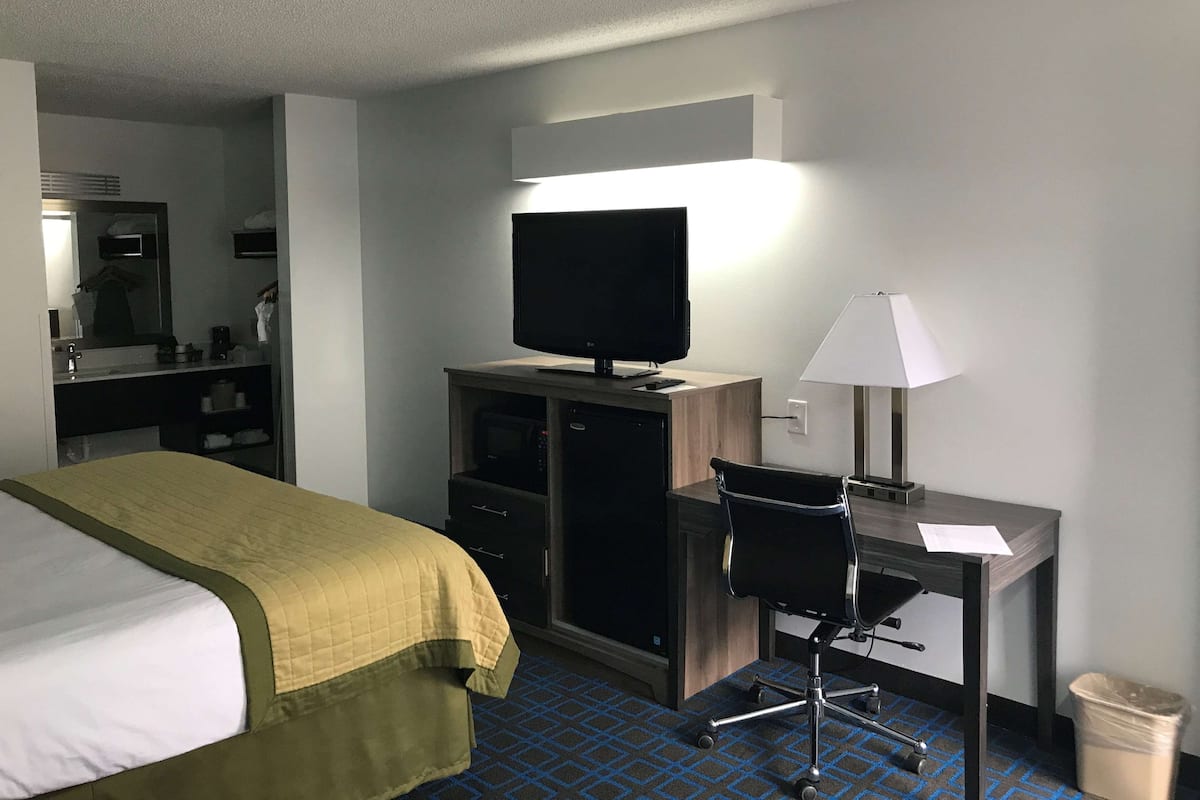 Une chambre d’hôtel avec un lit, un bureau équipé d’un ordinateur, une télévision et une lampe.