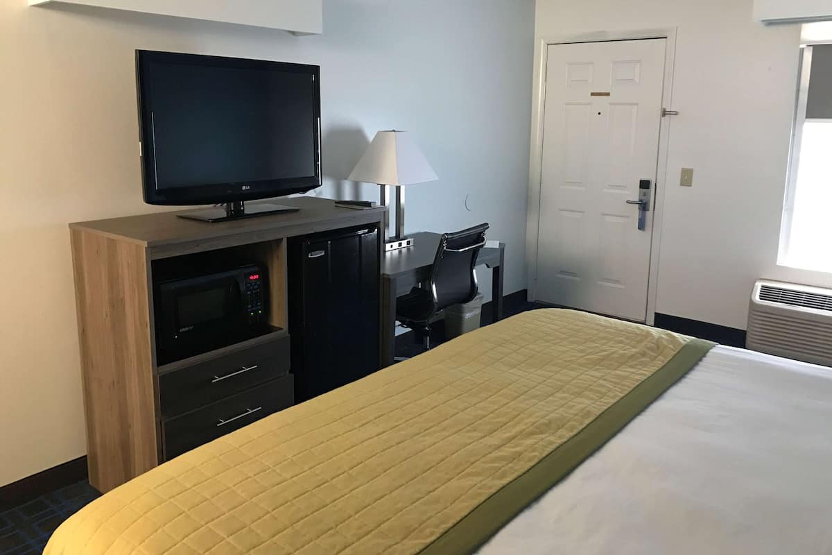 Une chambre d’hôtel équipée d’un lit, d’une télévision, d’un bureau avec une lampe, d’un four à micro-ondes et d’une porte.