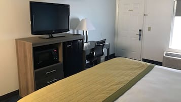Habitación de hotel con cama, televisión, escritorio con lámpara, microondas y puerta.