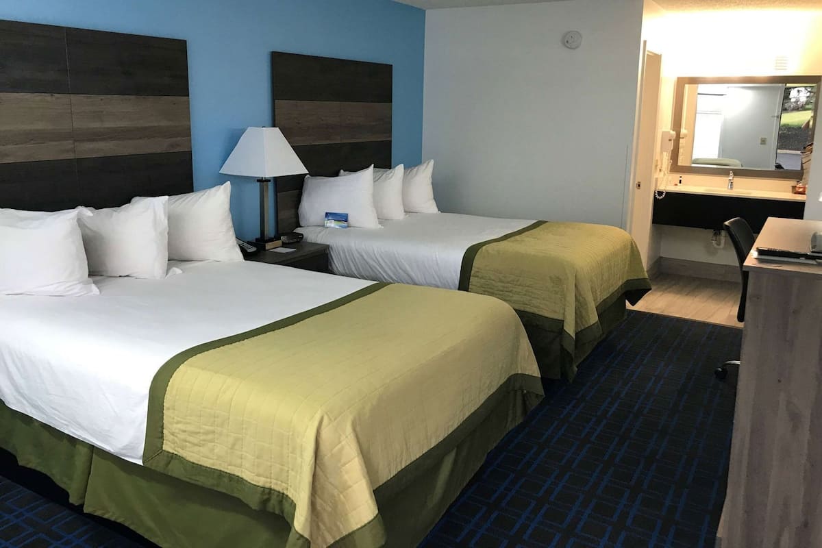 Une chambre d’hôtel avec deux lits, un bureau, une lampe et un miroir.