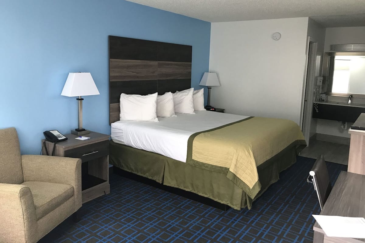 Une chambre d’hôtel comprenant un lit, deux tables de chevet, une chaise, un bureau, un miroir et une salle de bain.