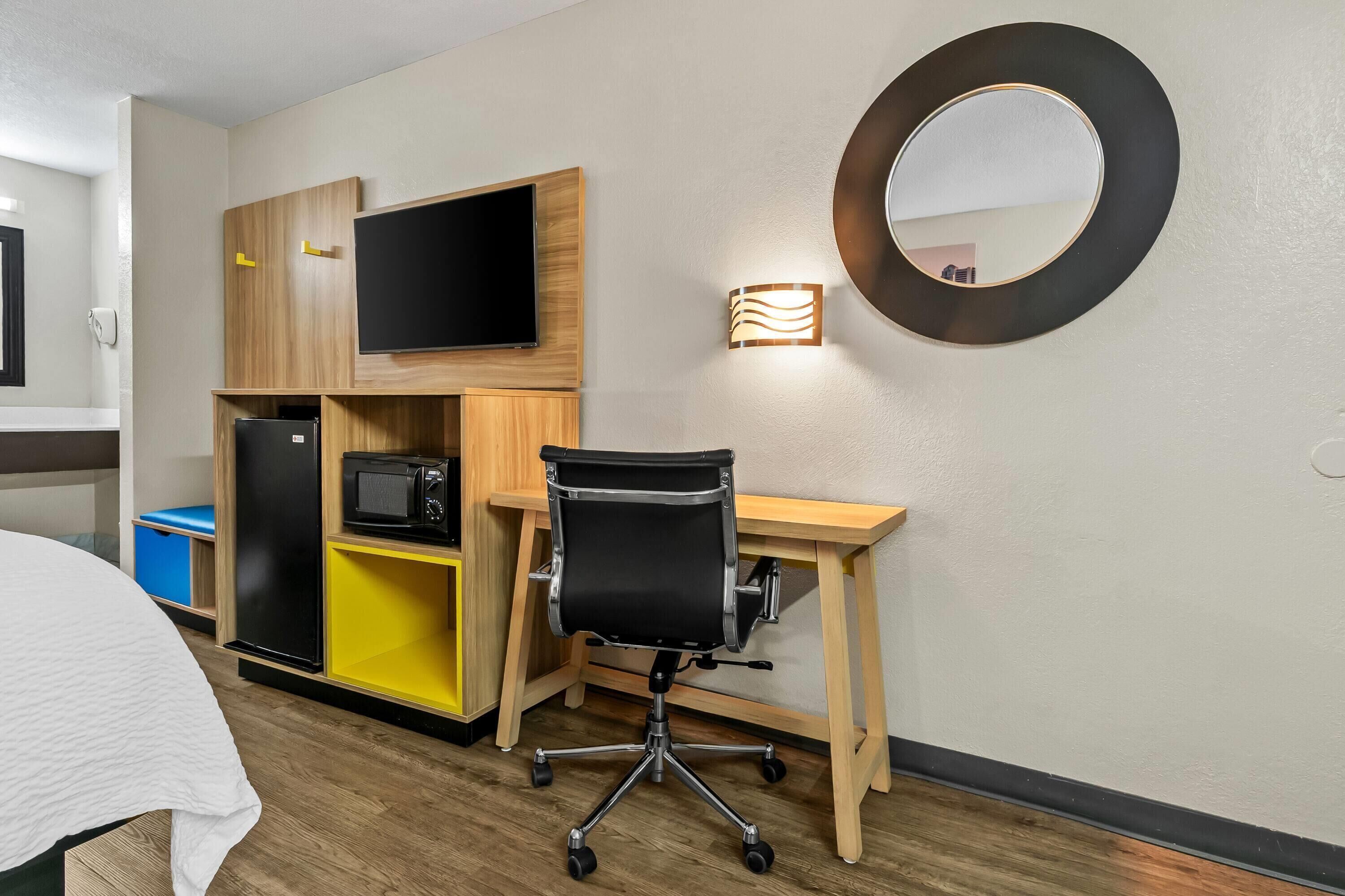 Une chambre d’hôtel équipée d’un lit, d’un bureau avec une chaise, d’un téléviseur à écran plat, d’un four à micro-ondes et d’un petit réfrigérateur.