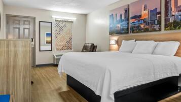 A hotel room with a large bed, a wardrobe, a desk, and a cityscape painting on the wall.
