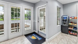 A hotel entrance with a doormat, an ATM, and a snack vending machine. - Days Inn by Wyndham Simpsonville (Simpsonville)