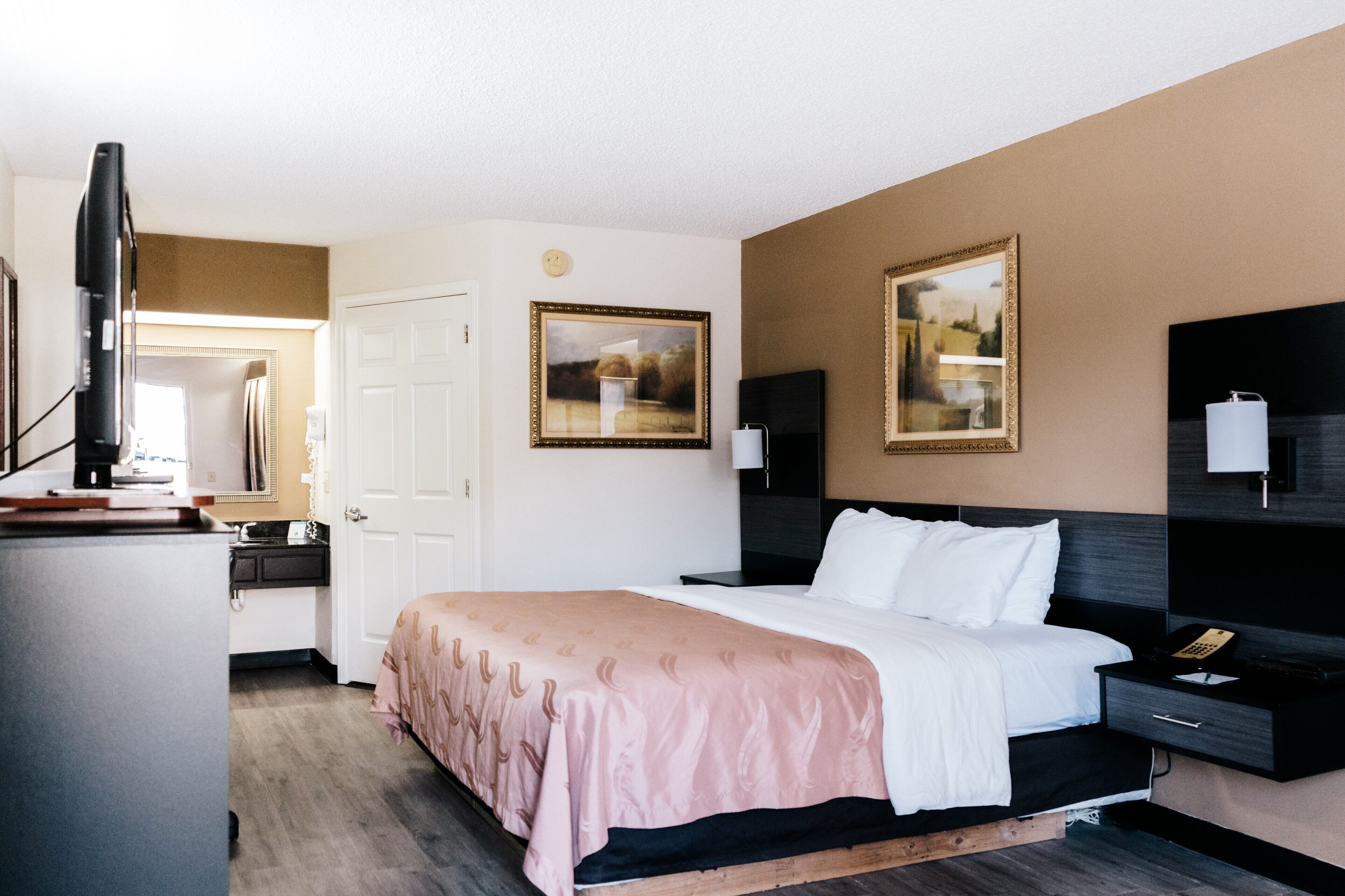 Une chambre d’hôtel avec un lit, des tables de chevet, une télévision et deux tableaux encadrés au mur.
