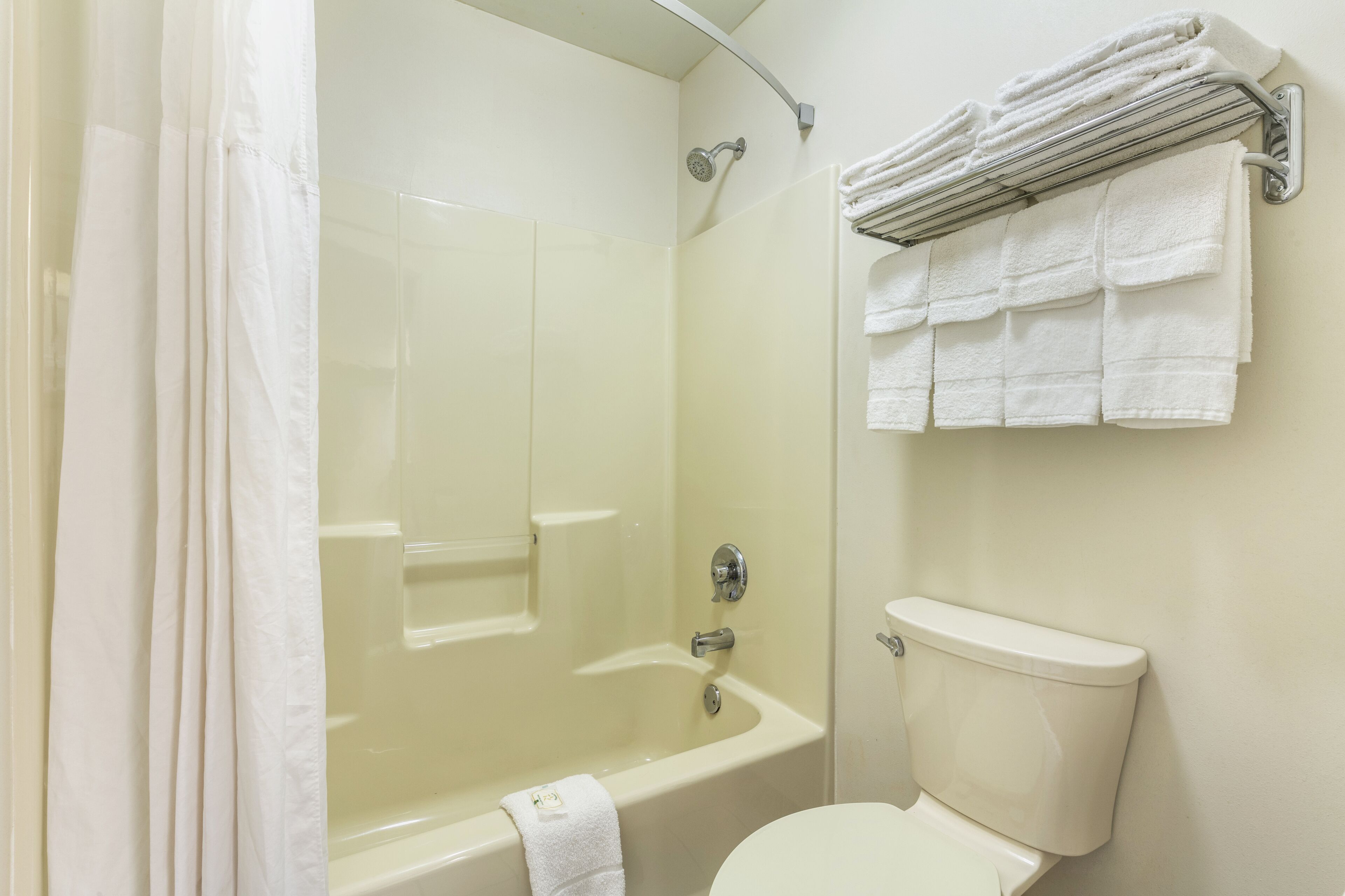 A bathroom with a bathtub, shower, and toilet. There are towels on a rack and a shower curtain.
