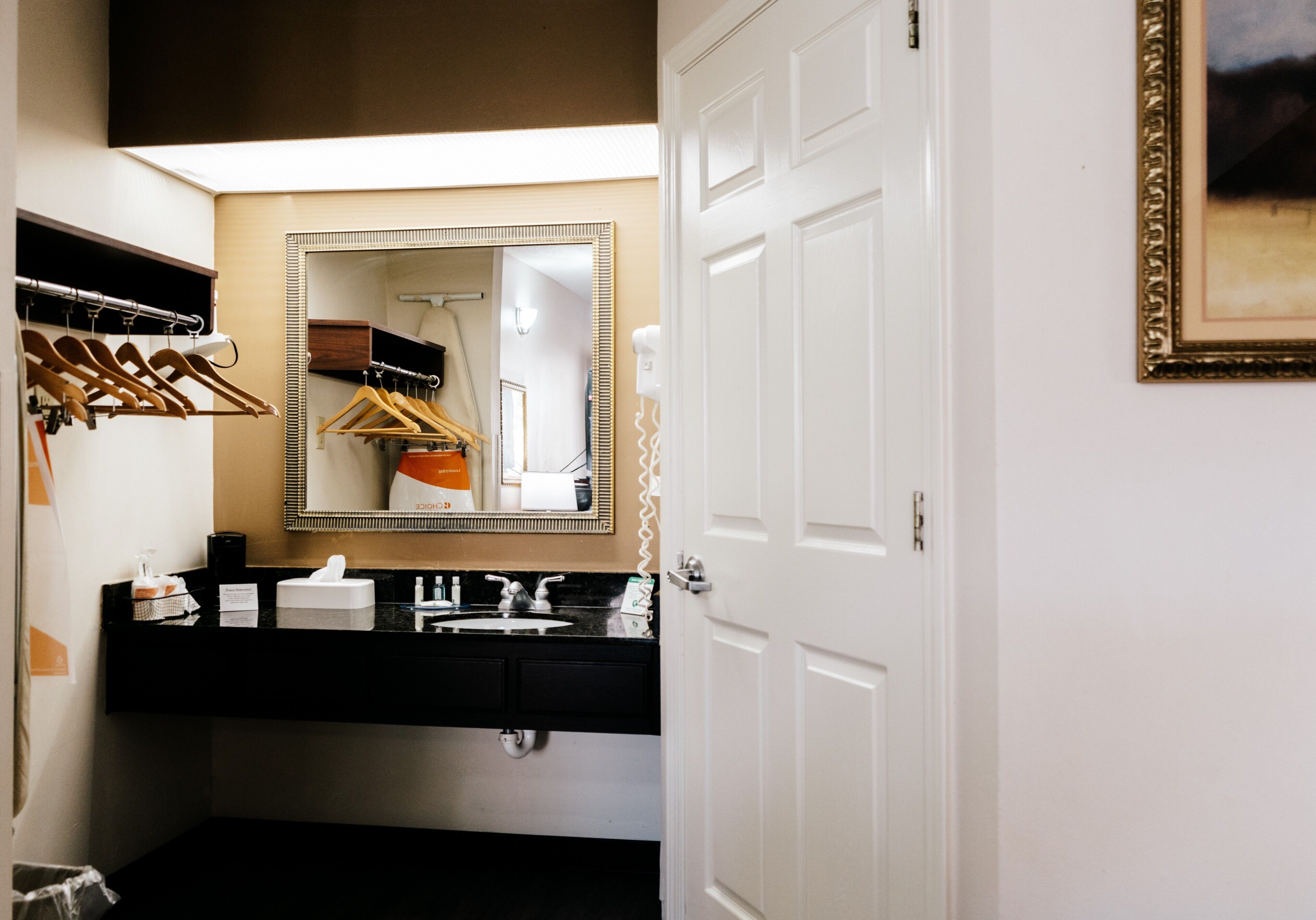 Un baño de hotel con tocador negro, un espejo grande y una puerta blanca.