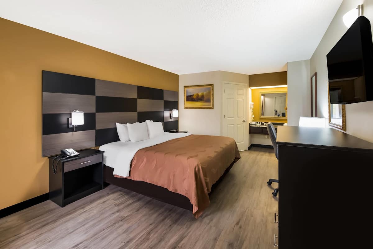 Una habitación de hotel con cama, mesita de noche, lámpara y escritorio con silla.