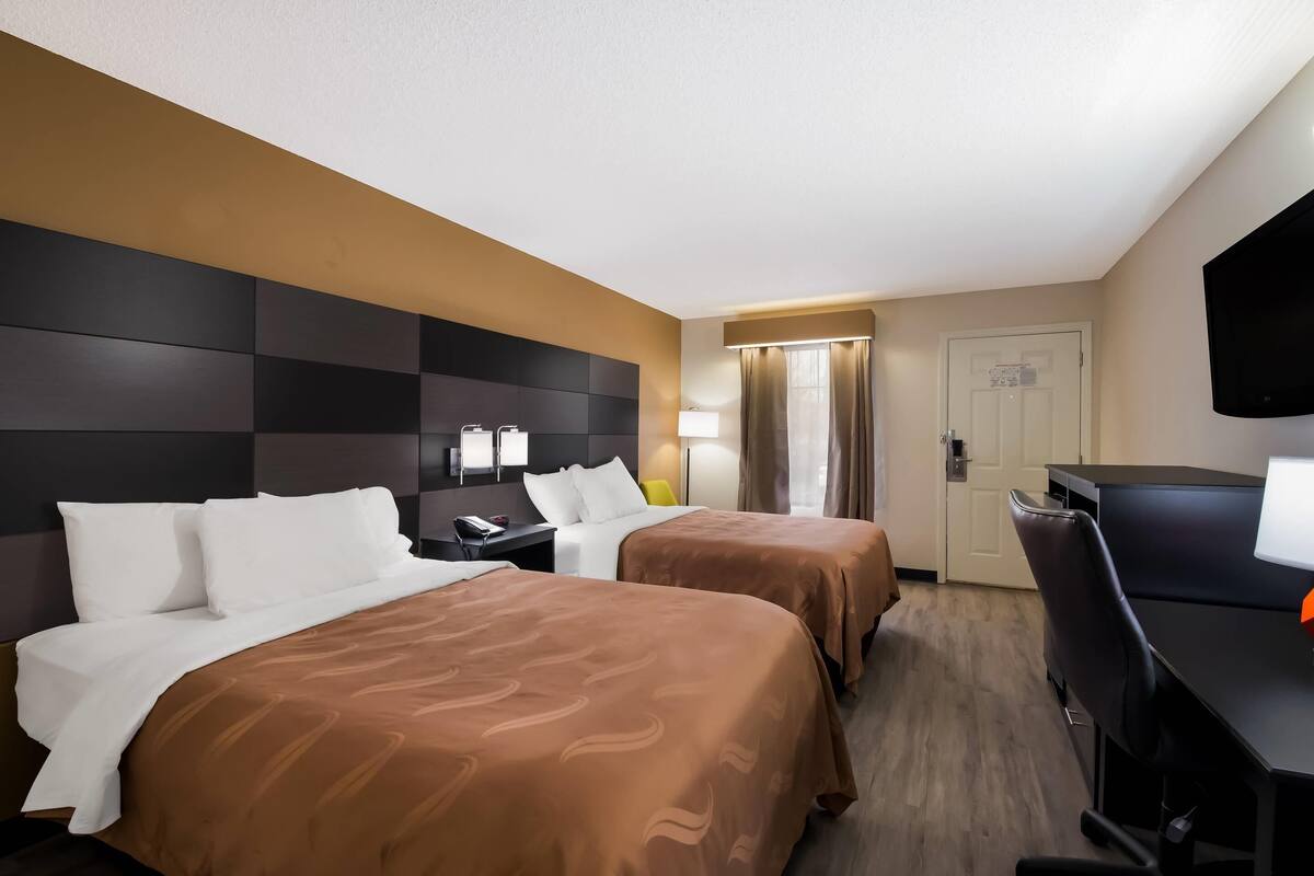 Una habitación de hotel con dos camas, un escritorio, una silla, un televisor y una puerta.