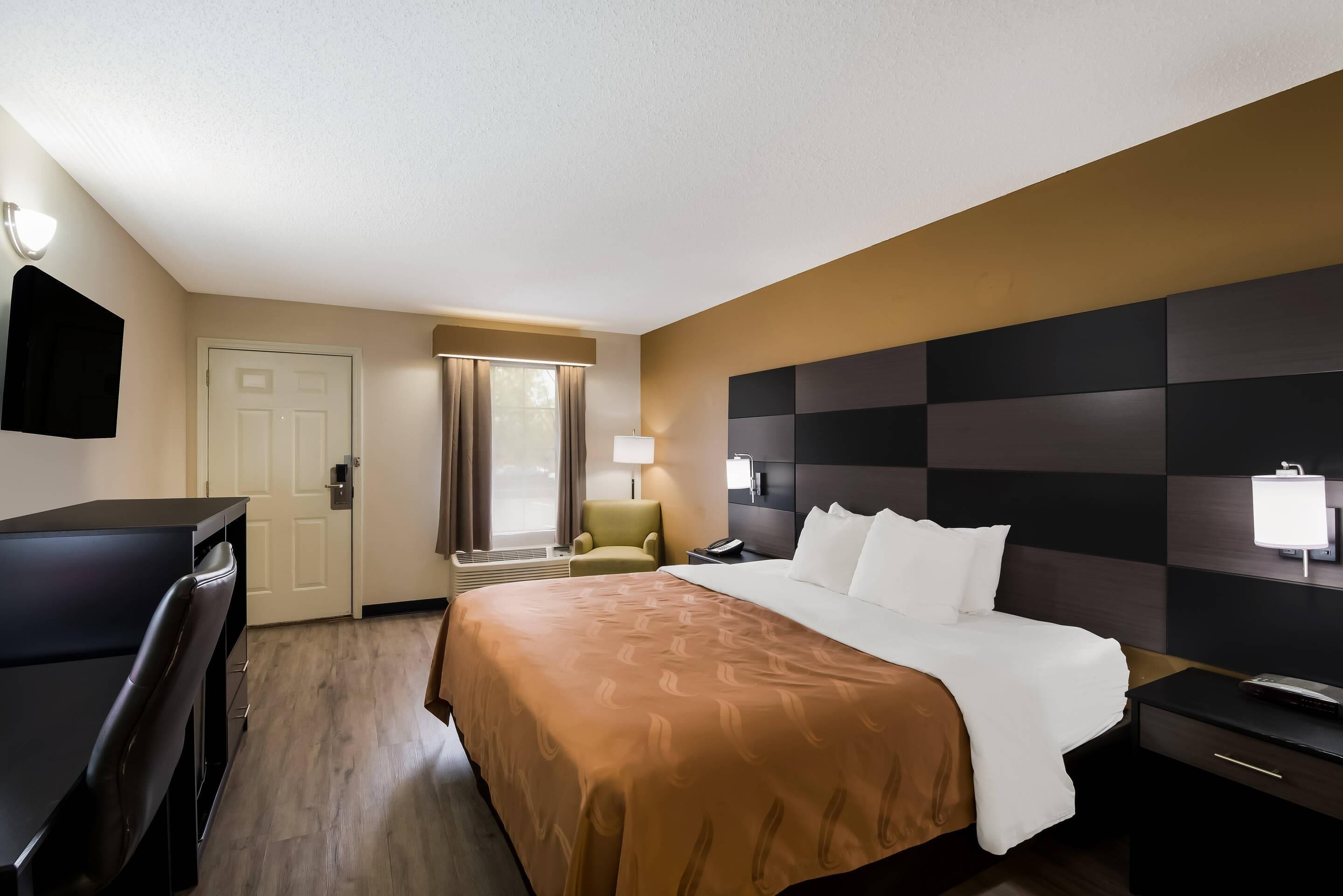 Une chambre d’hôtel avec un lit, un bureau, une chaise, une télévision et une fenêtre avec des rideaux.