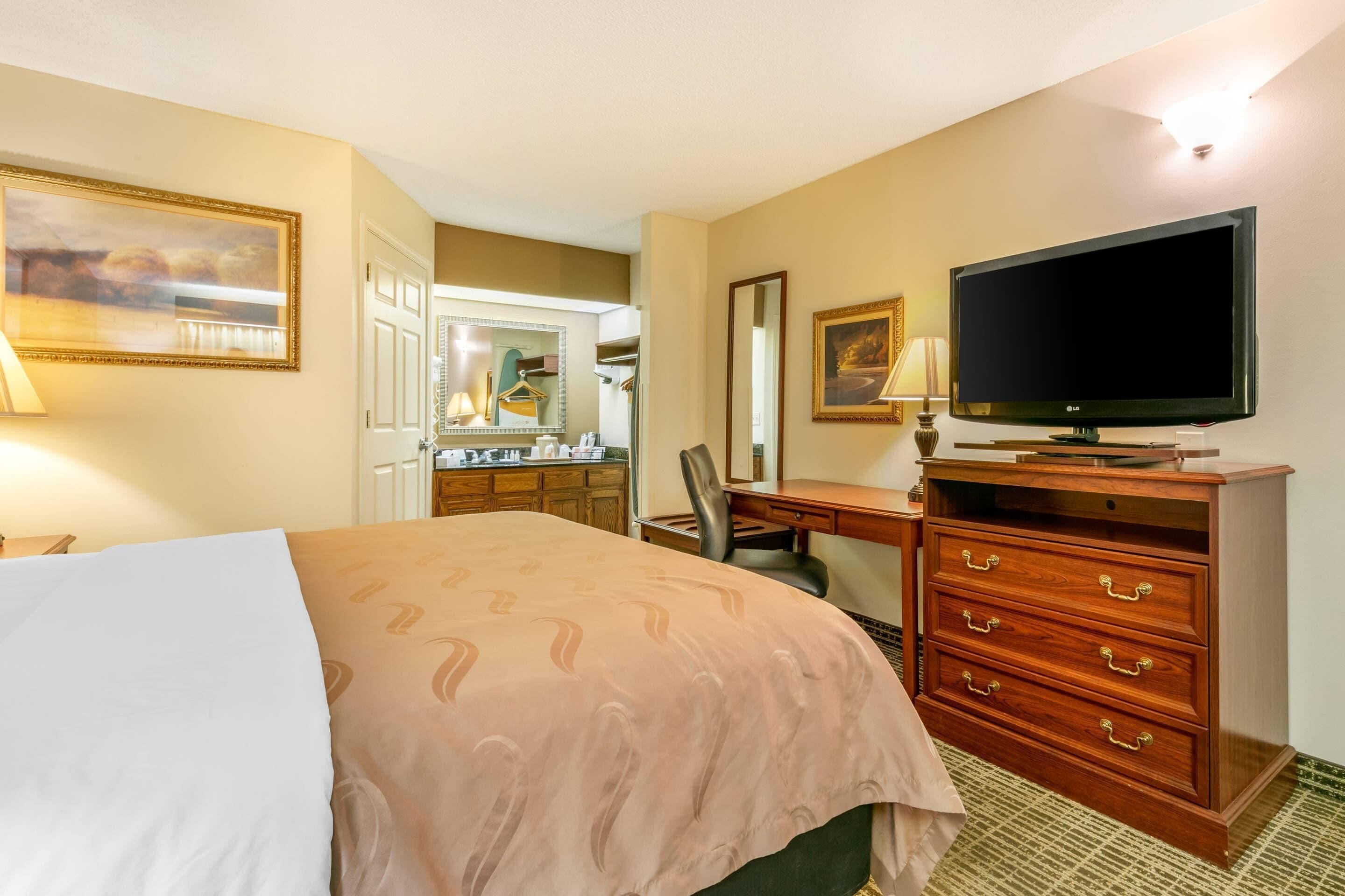 Une chambre d’hôtel équipée d’un lit, d’une télévision, d’une commode, d’un bureau et d’un miroir.
