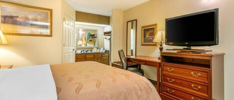 Une chambre d’hôtel équipée d’un lit, d’une télévision, d’une commode, d’un bureau et d’un miroir.