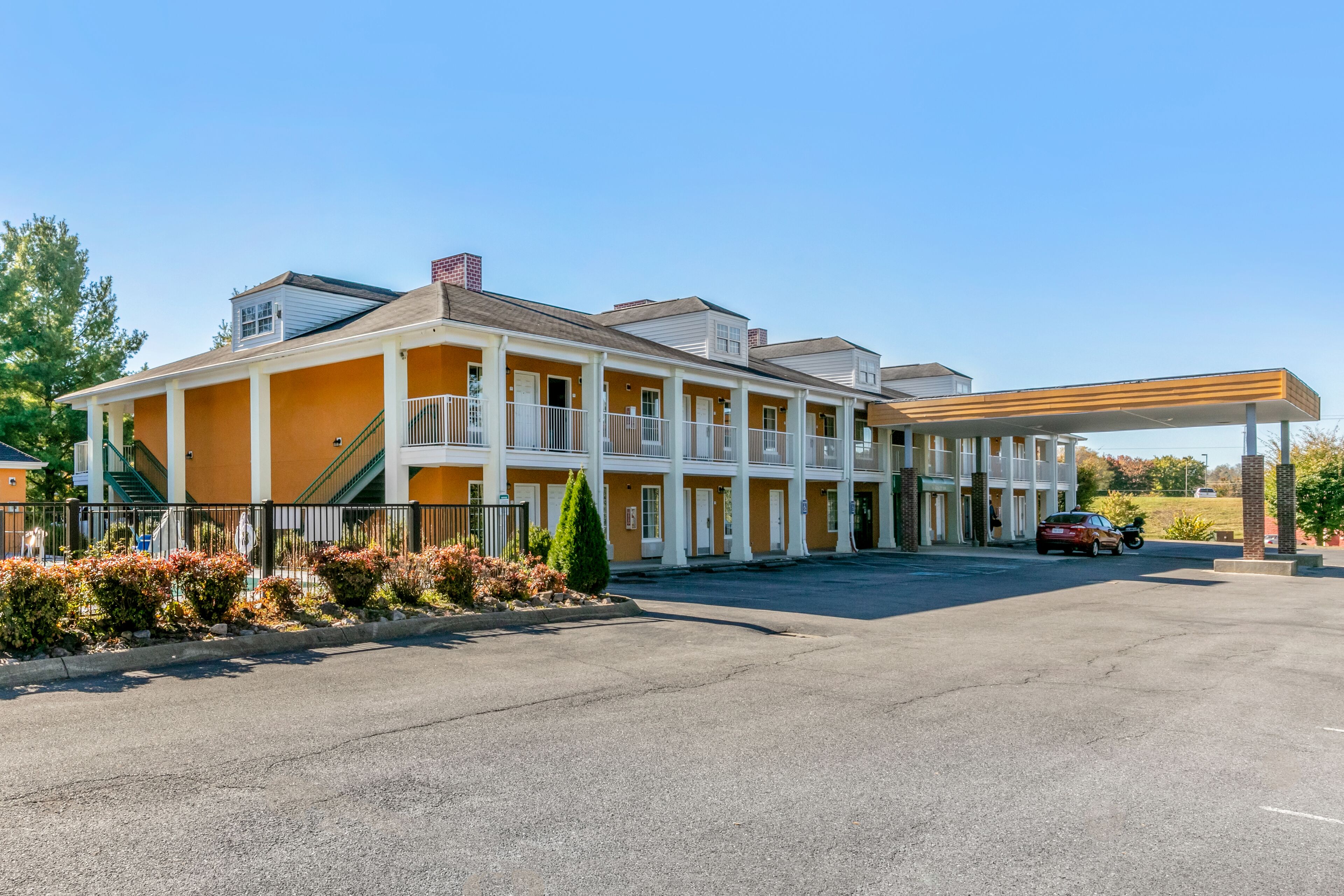 Un motel con área de estacionamiento techada y una construcción de un solo piso.