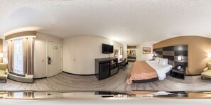 A panoramic view of a hotel room with a curved ceiling, a bed, a desk with a chair, a television, and a nightstand with a lamp.