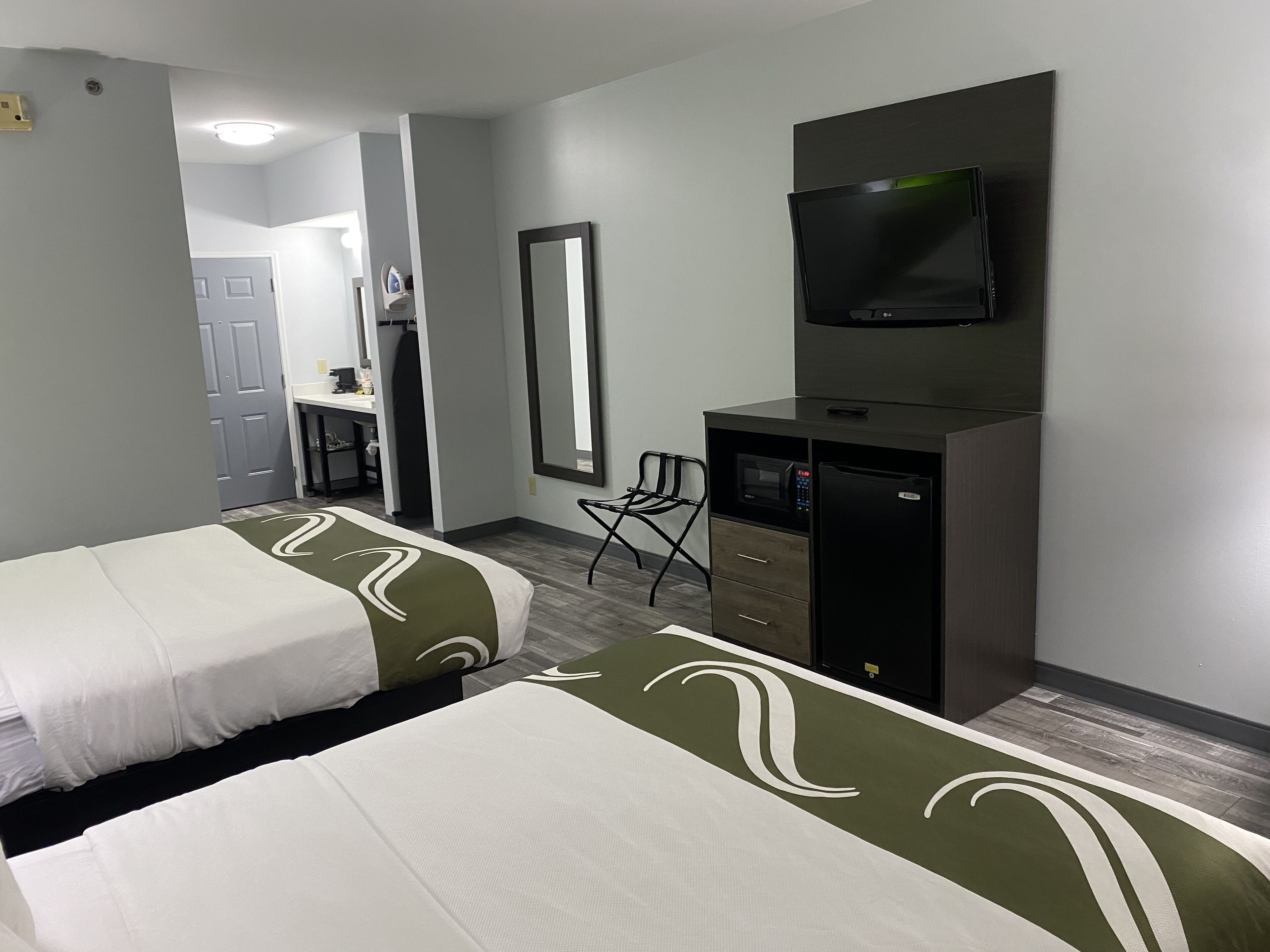 Habitación de hotel con dos camas, un escritorio, una silla, un televisor y un armario.