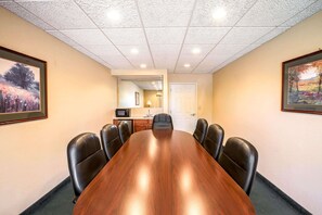 Ein Konferenzraum mit einem langen Holztisch, sechs schwarzen Ledersesseln, einer weißen Tür und gerahmten Bildern an den Wänden.