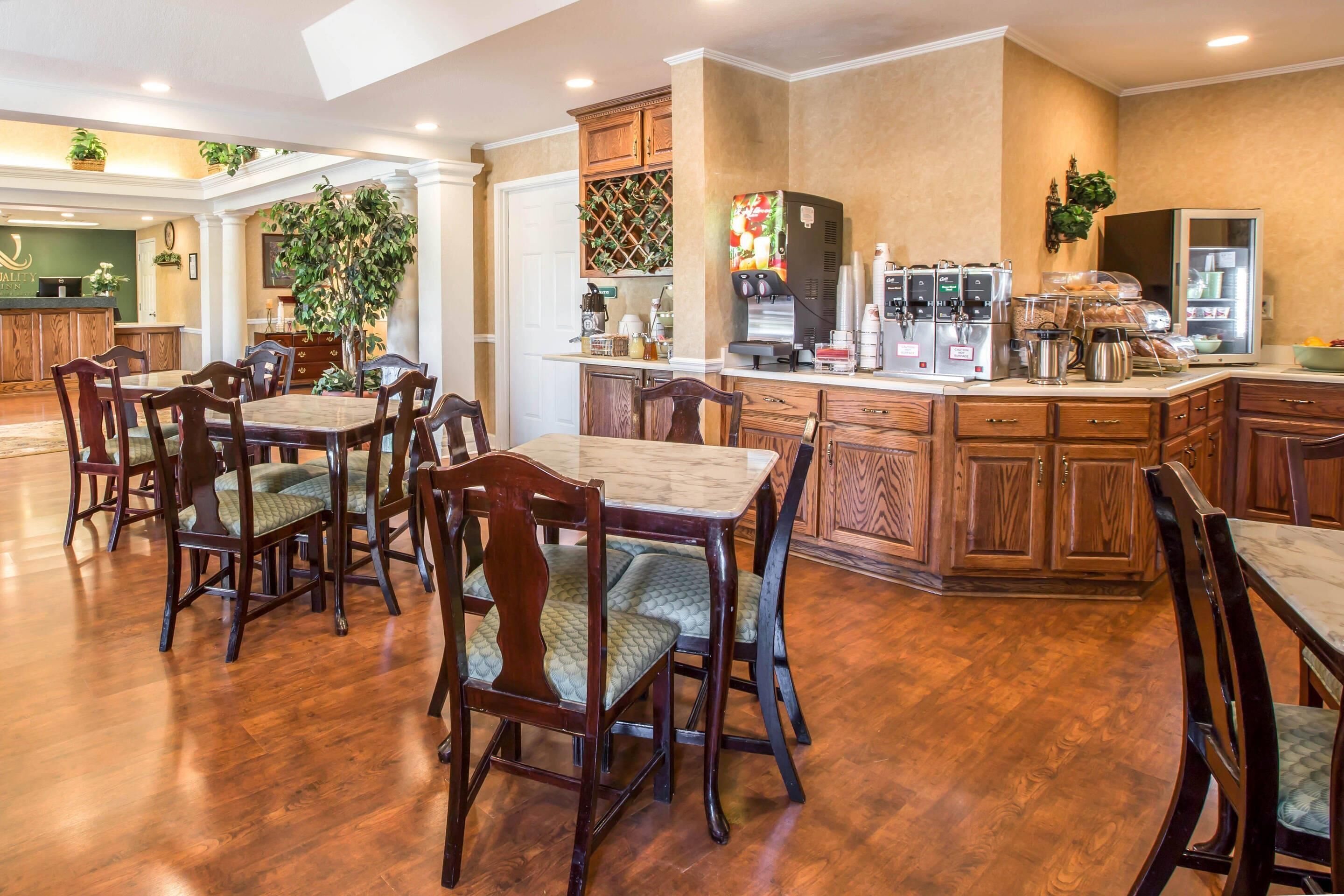 Un comedor de hotel con mobiliario de madera, una cocina con máquinas de café y un mostrador de recepción.