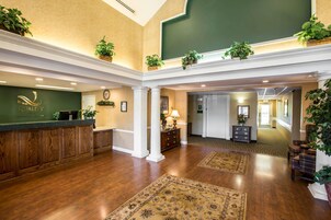 A hotel lobby with a reception desk, a clock, and a green wall with a sign.