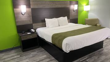 Quarto de hotel moderno com uma cama grande, uma mesa de cabeceira com telefone e uma luminária.