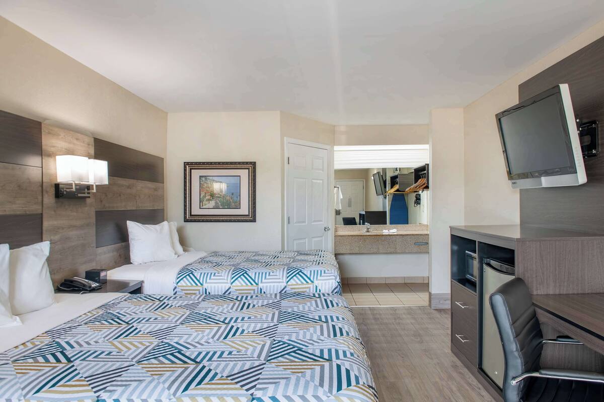 Une chambre d’hôtel avec un grand lit, un bureau avec une chaise, une télévision, un miroir et une porte donnant sur une salle de bain.