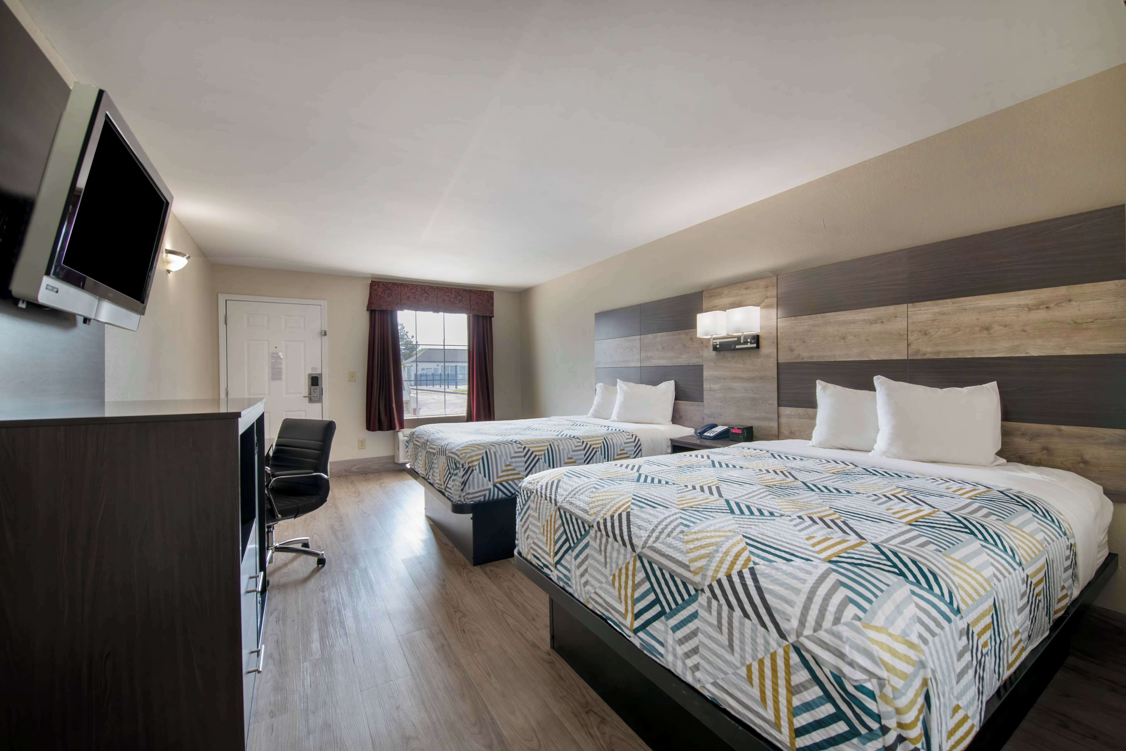 Habitación de hotel con dos camas, televisión, escritorio y ventana con cortinas.
