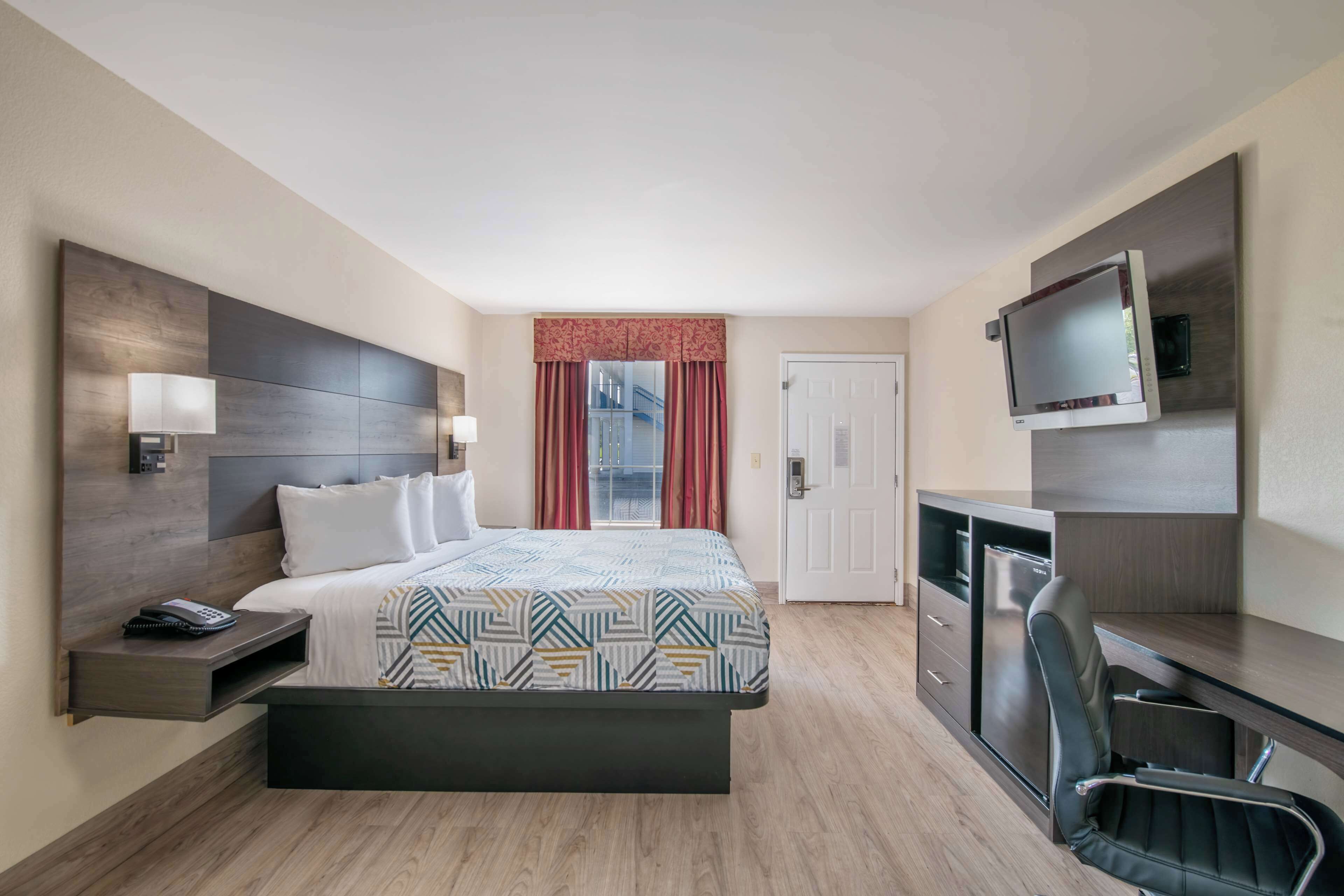 Een hotelkamer met een bed, nachtkastje, televisie, bureau en stoel.