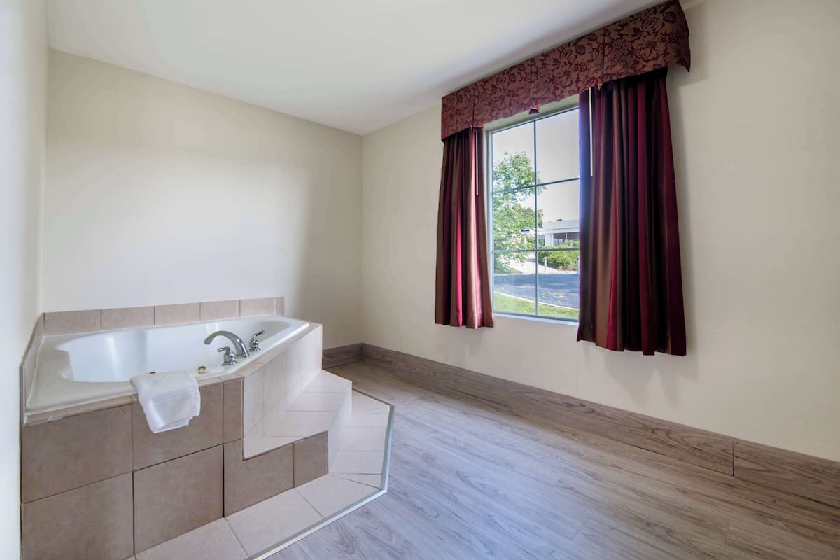 Une salle de bain avec une baignoire sur pieds, une fenêtre avec des rideaux rouges et une vue sur l’extérieur.