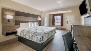 Une chambre d’hôtel avec un grand lit, un bureau, un téléviseur à écran plat et une fenêtre avec des rideaux.