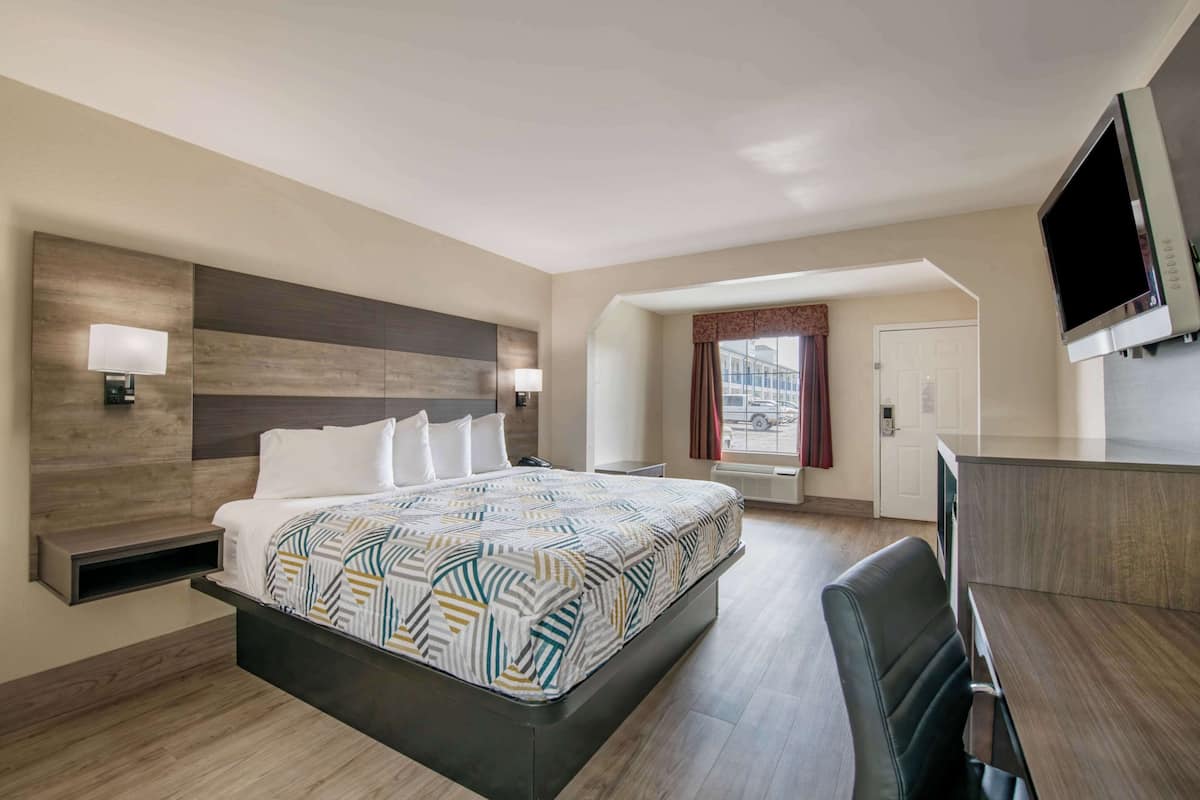 Une chambre d’hôtel avec un grand lit, un bureau, un téléviseur à écran plat et une fenêtre avec des rideaux.