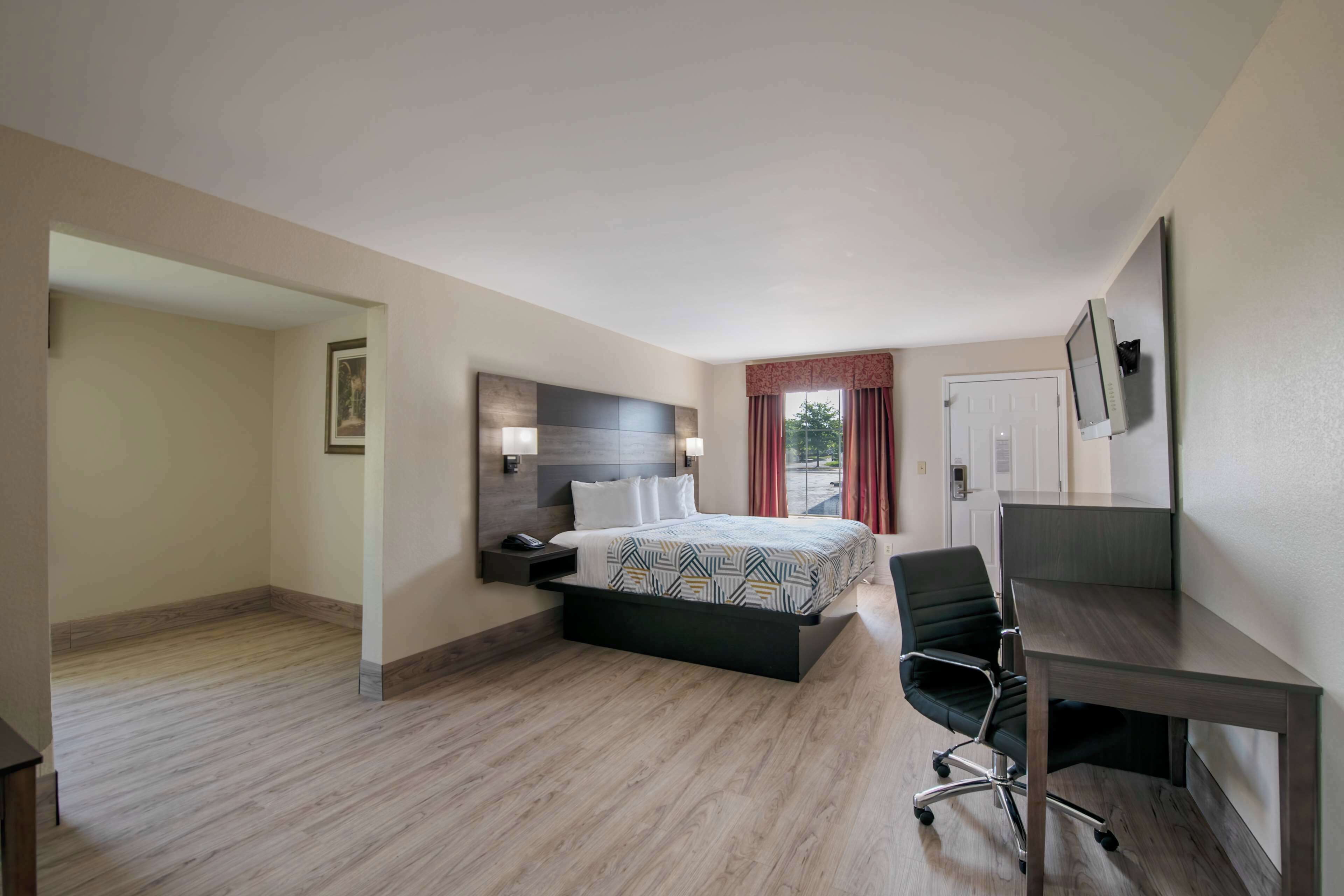 A hotel room with a bed, a desk, a chair, a nightstand, and a window with curtains.