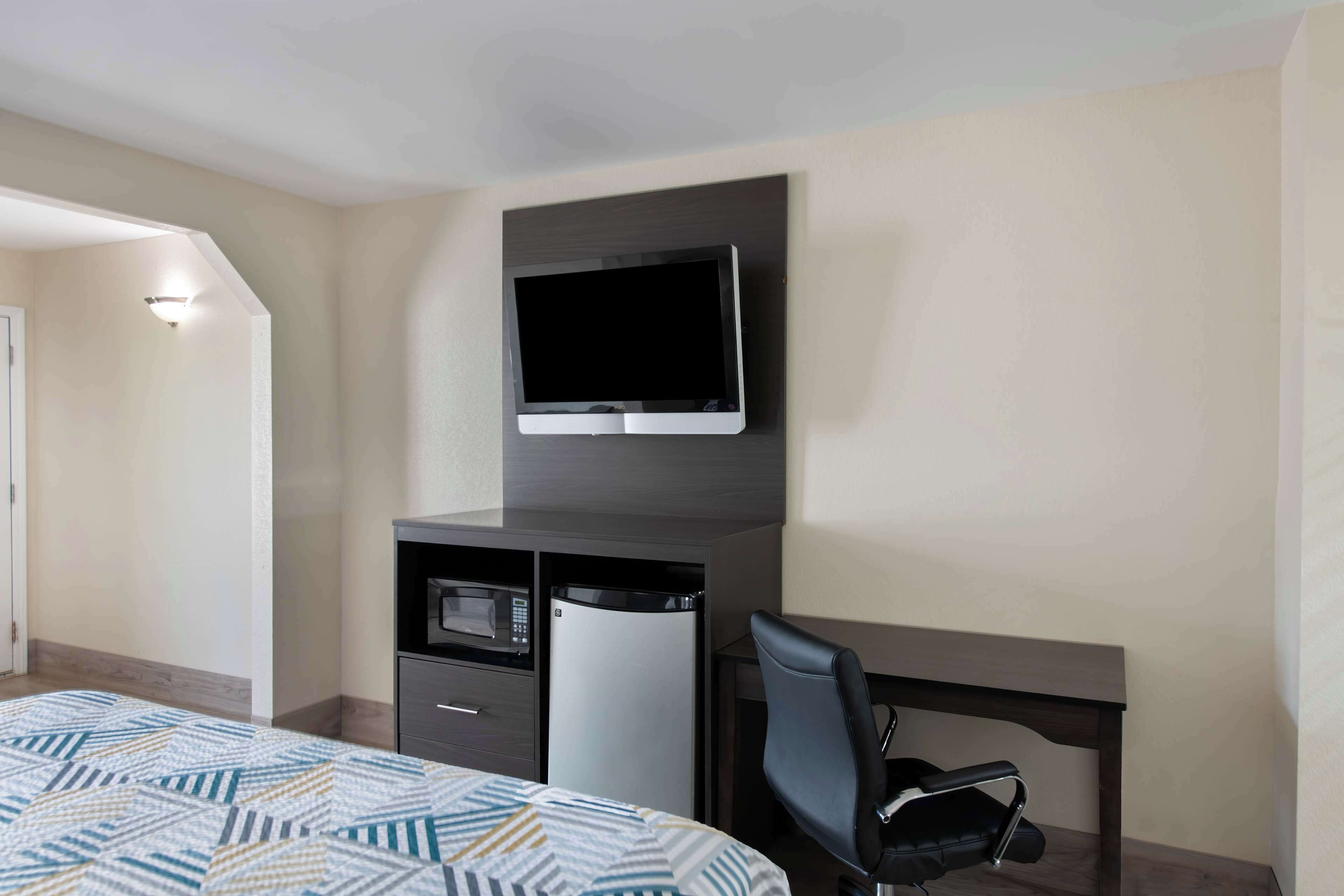 A hotel room with a bed, a desk with a chair, a television mounted on the wall, and a microwave.