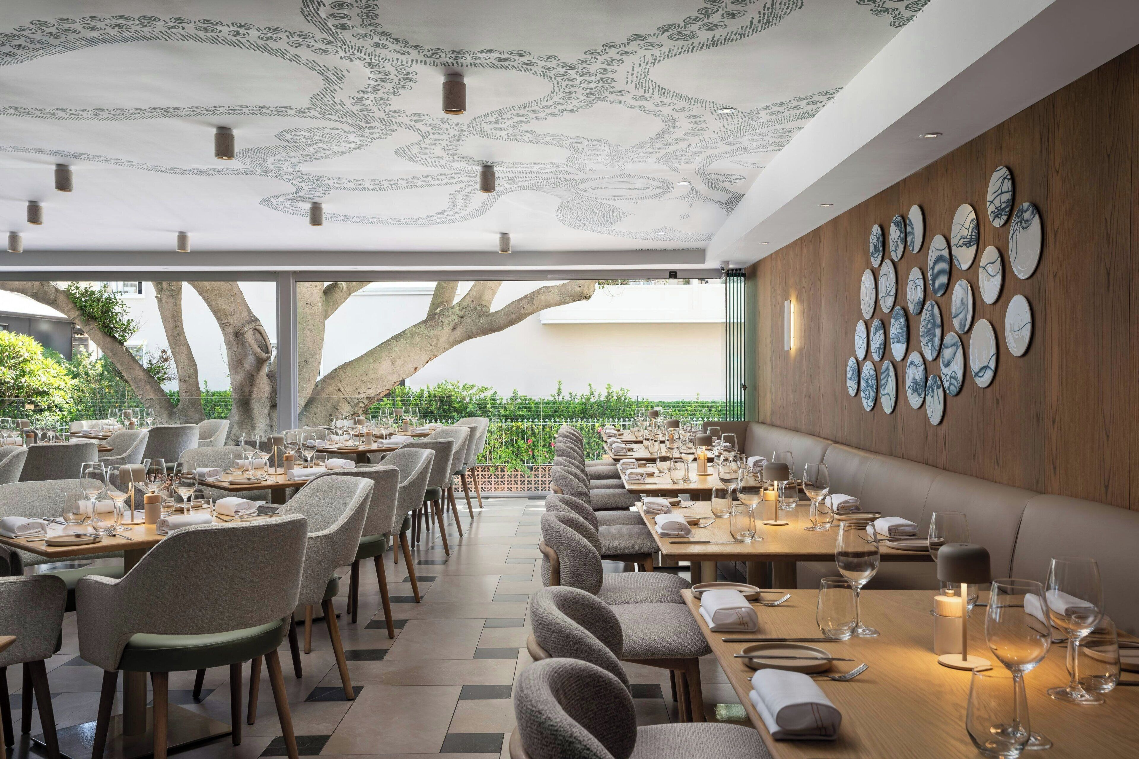 A restaurant with a long dining area, wooden walls, and a ceiling with a detailed pattern.