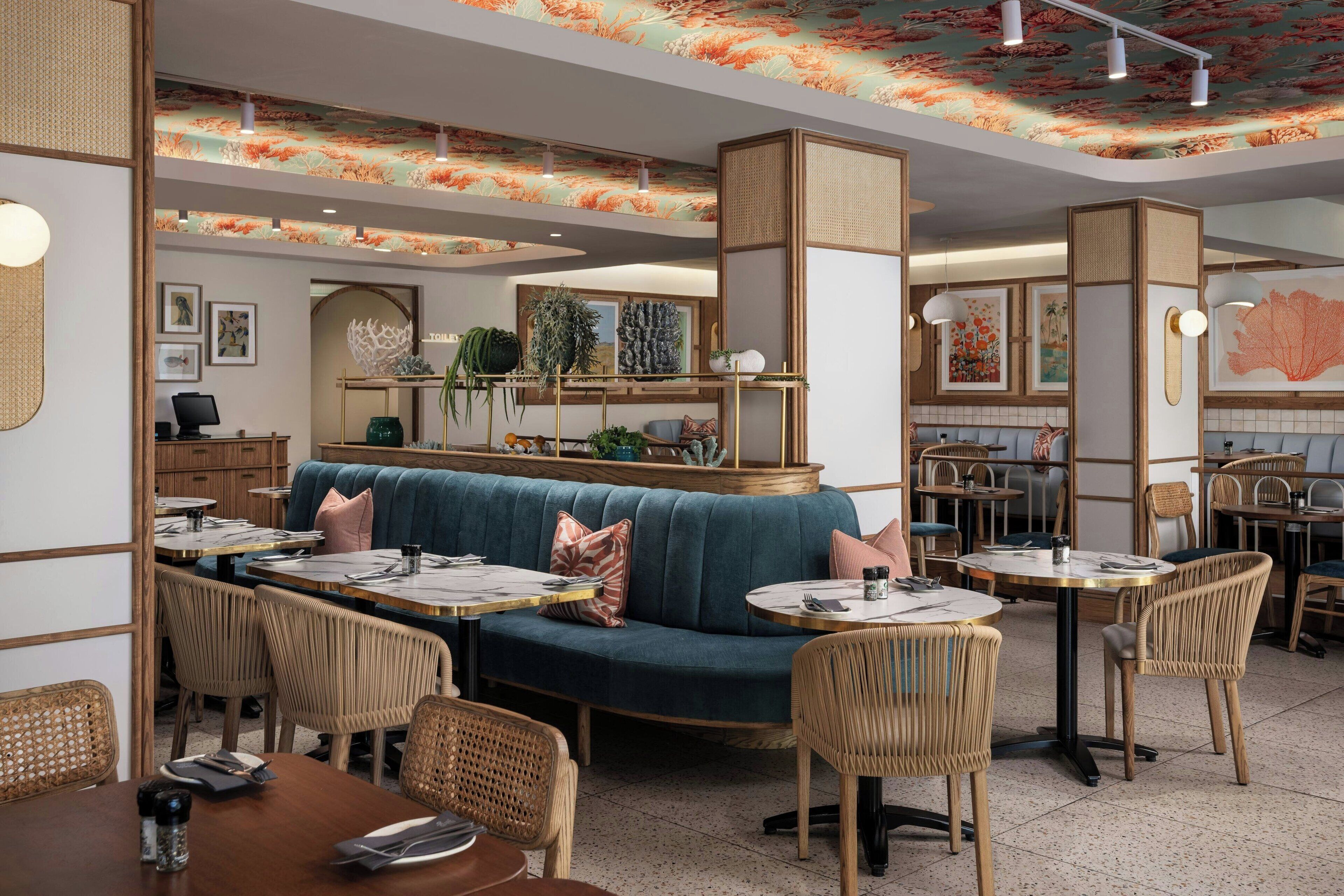 A restaurant interior with a blue sofa, wicker chairs, and round tables.