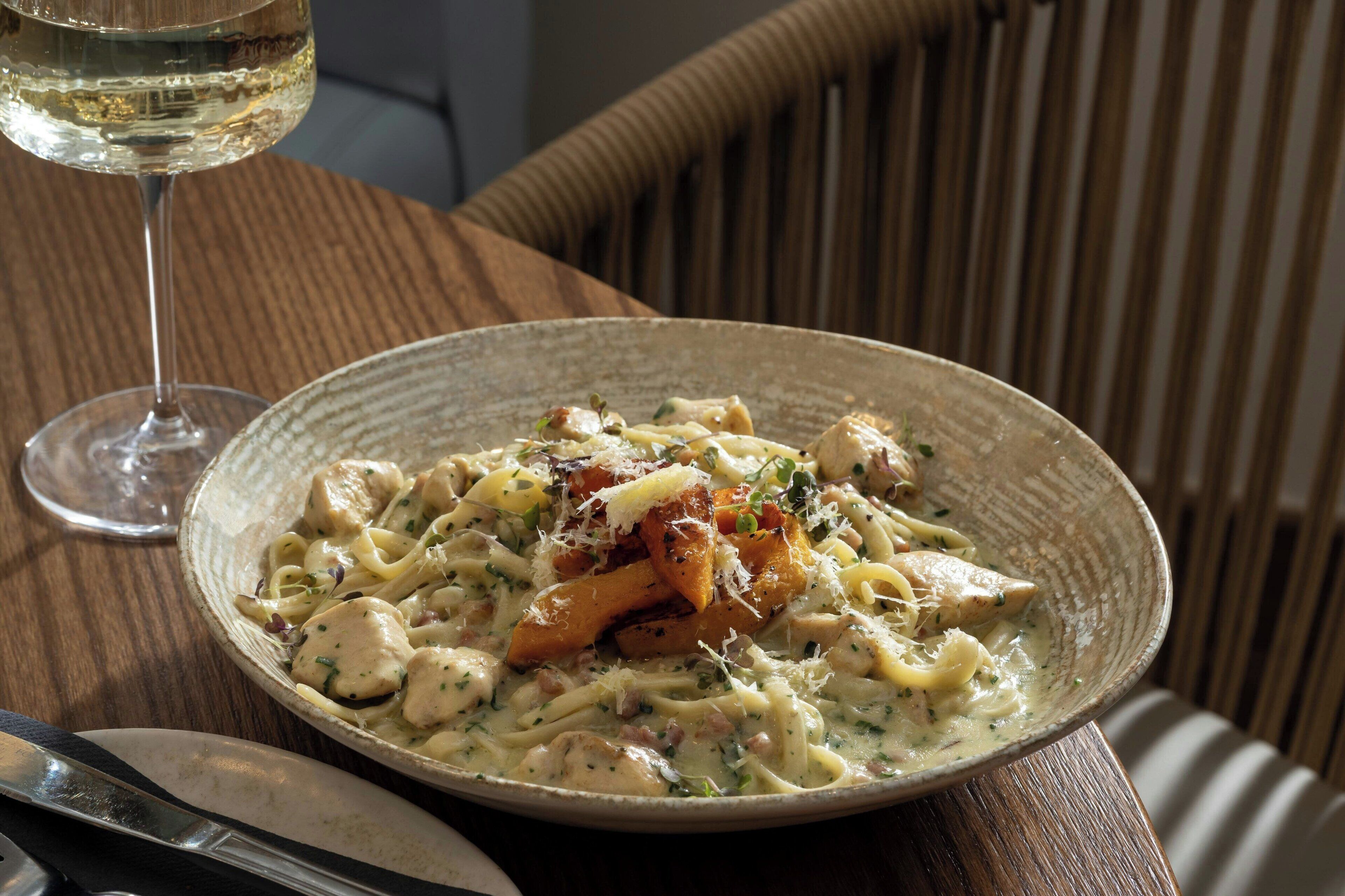 A plate of creamy pasta with chicken and cheese, accompanied by a glass of white wine, on a wooden table.