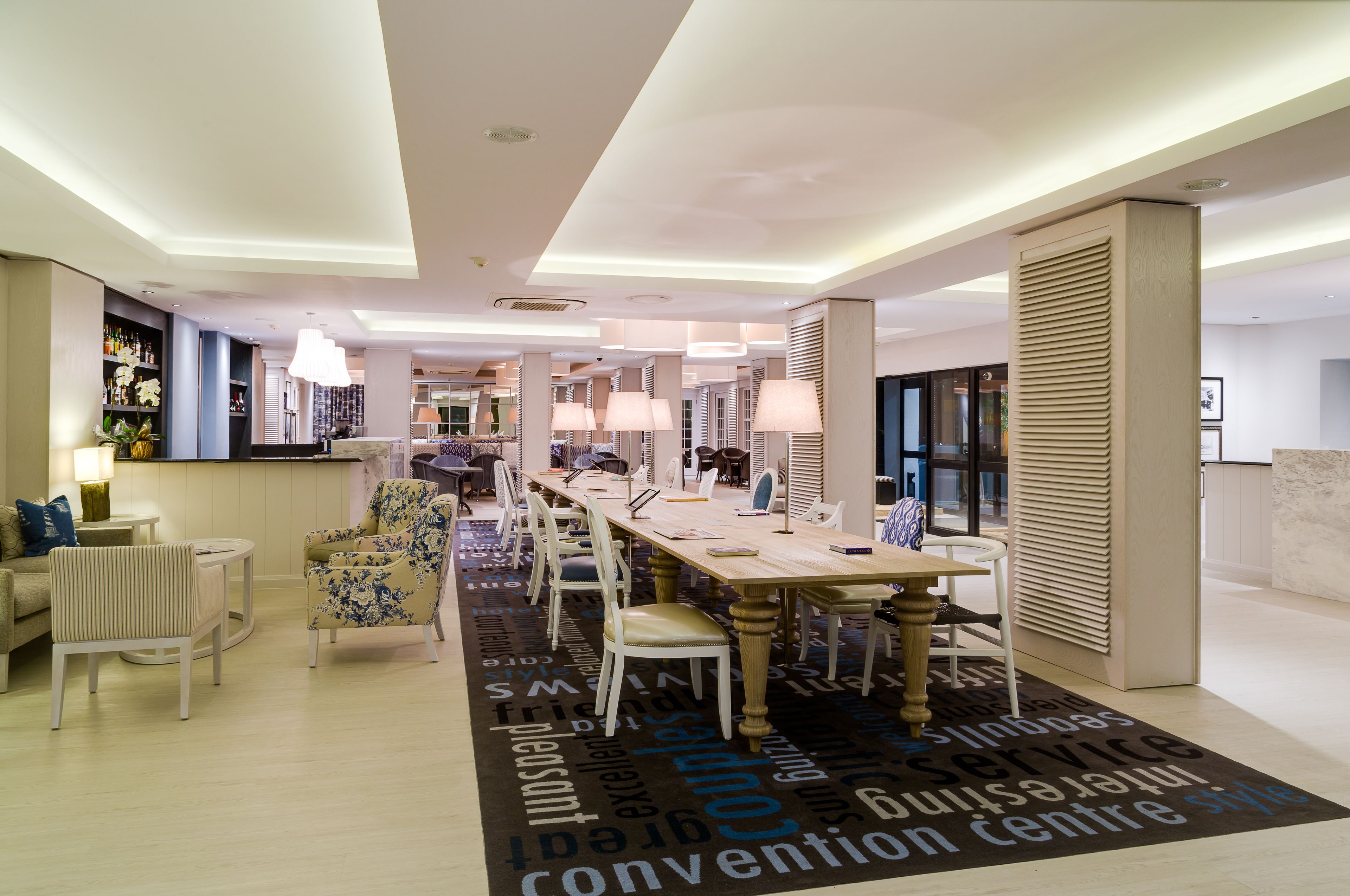Un hall d’hôtel moderne avec un long comptoir d’accueil, des sièges confortables et une grande moquette ornée de mots tels que « centre de congrès » et « service ».