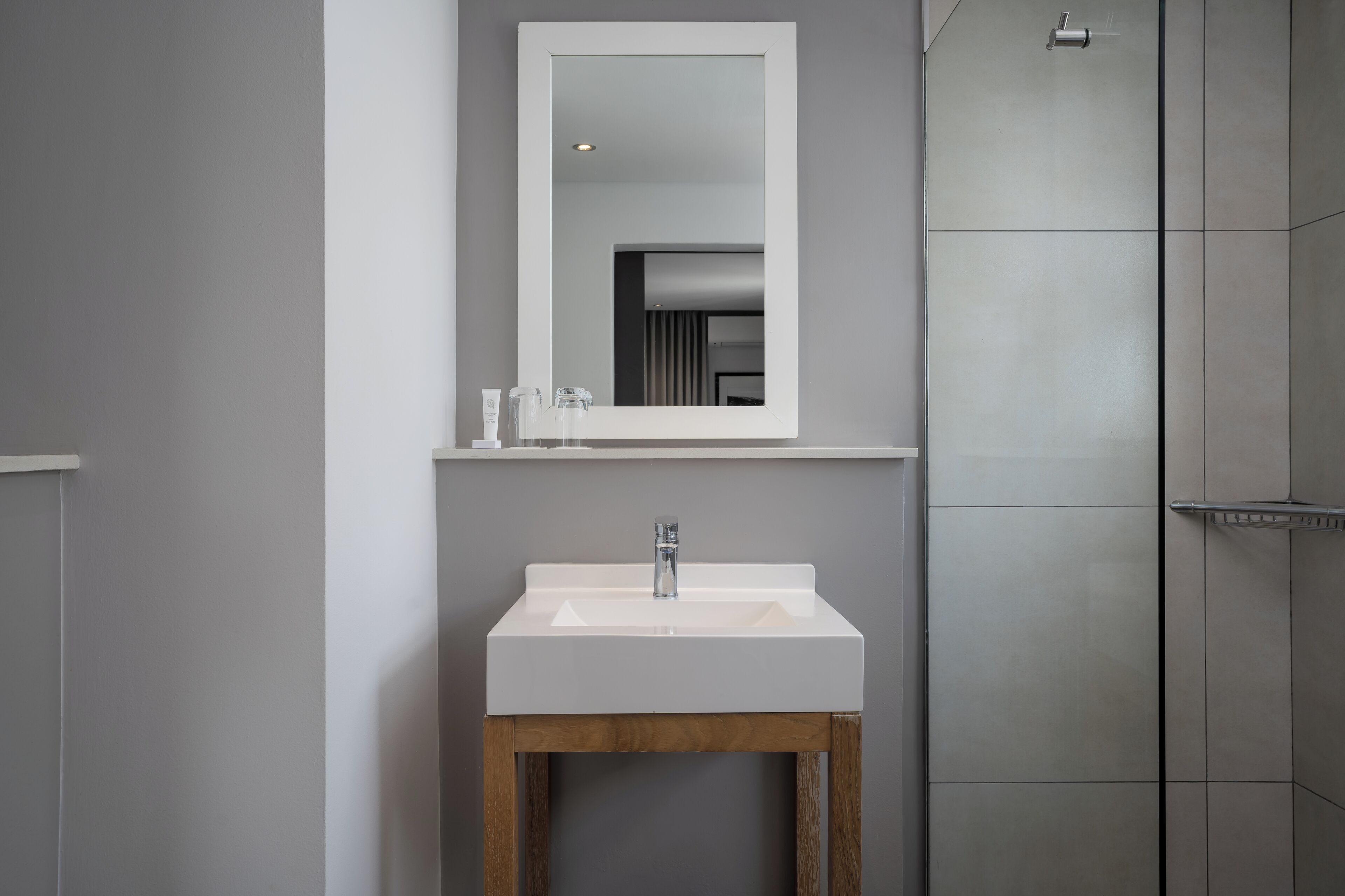 A modern bathroom with a white sink, wooden base, and a mirror above it.