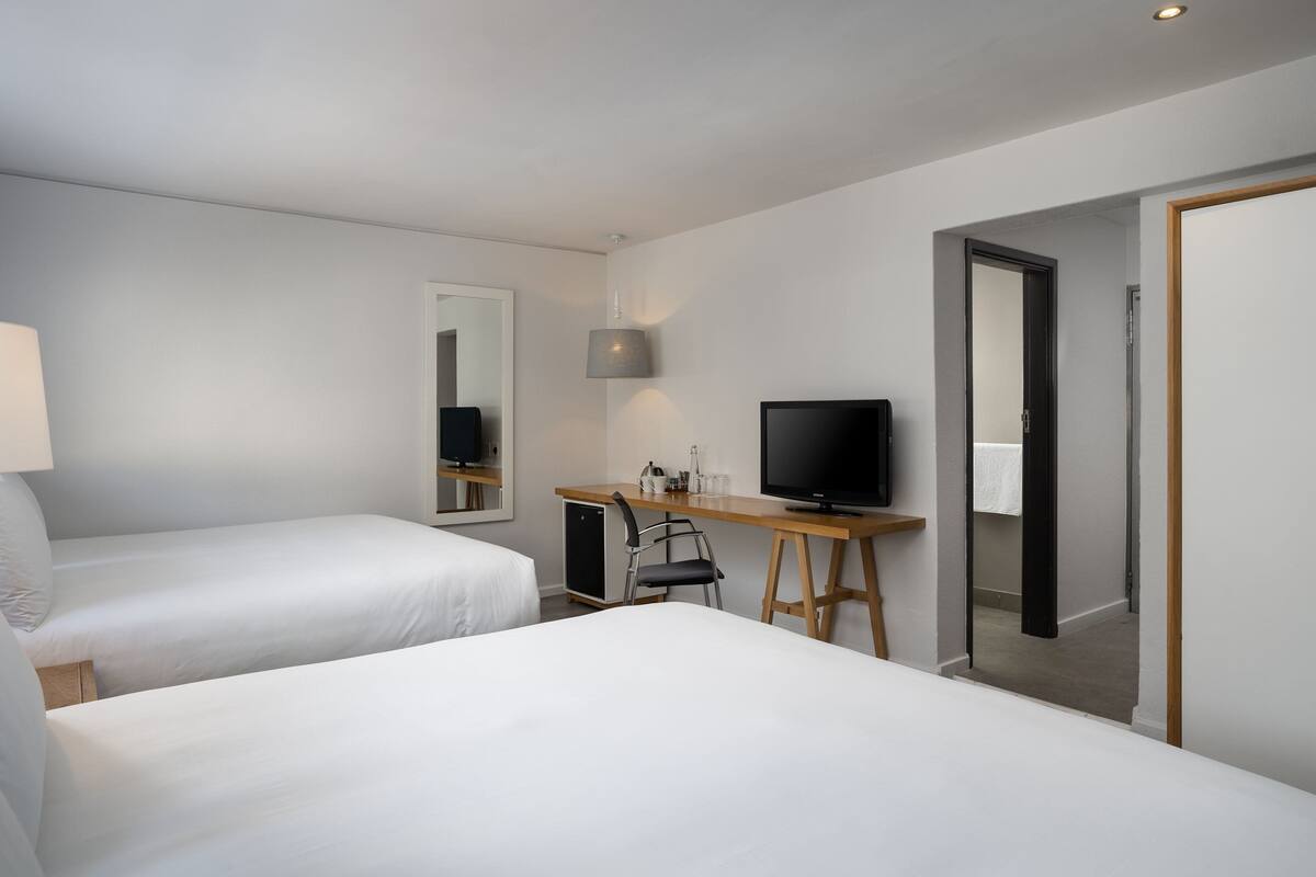 A hotel room with two beds, a desk with a television, a mirror, and a door leading to a bathroom.
